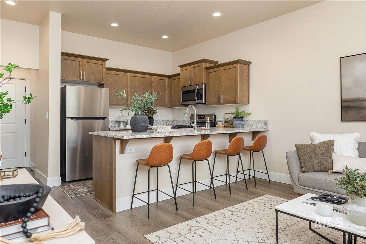 Kitchen featuring a kitchen bar, appliances with stainless steel finishes, light stone counters, brown cabinetry, and a peninsula