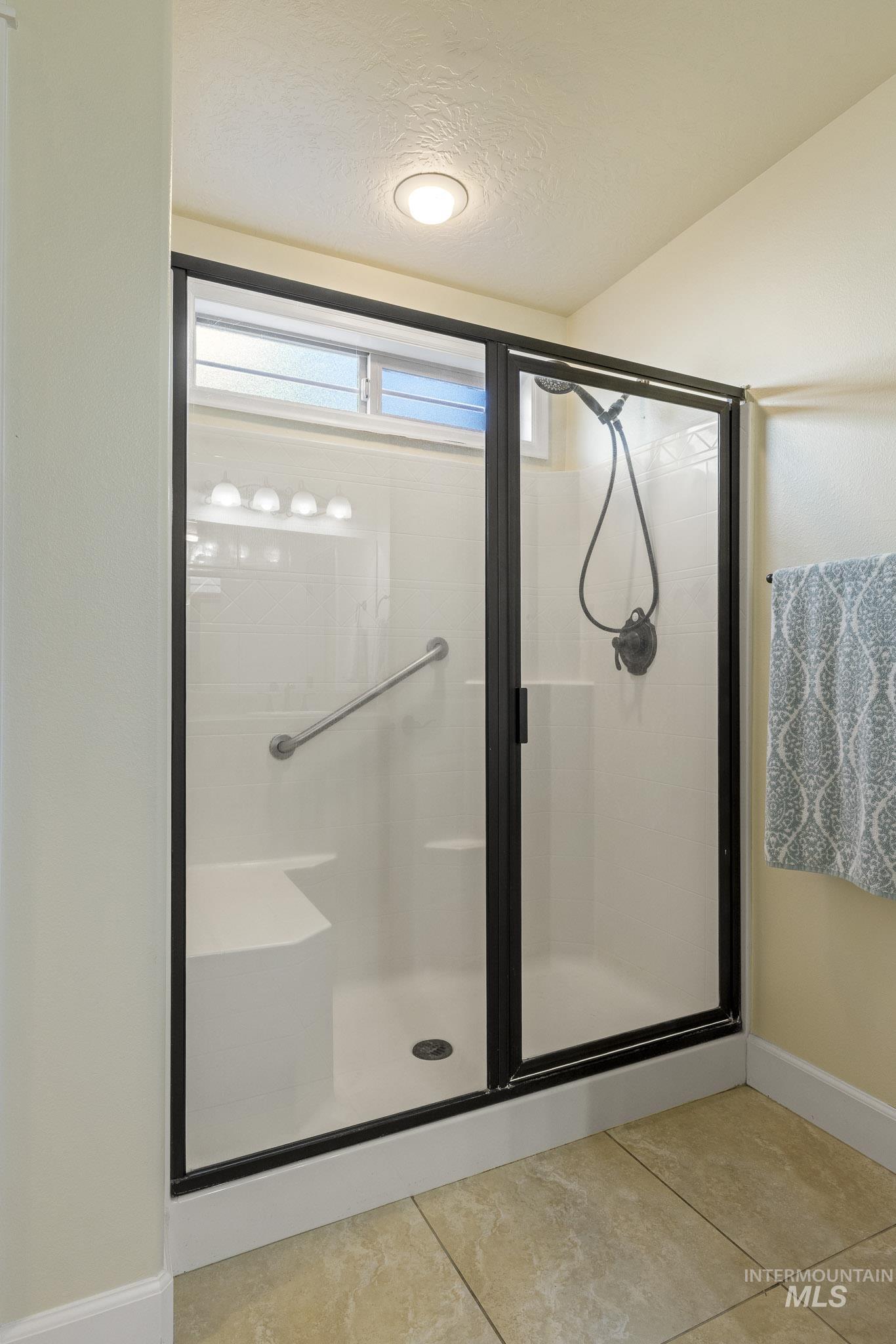 Full bathroom featuring a stall shower, a textured ceiling, and light tile patterned floors