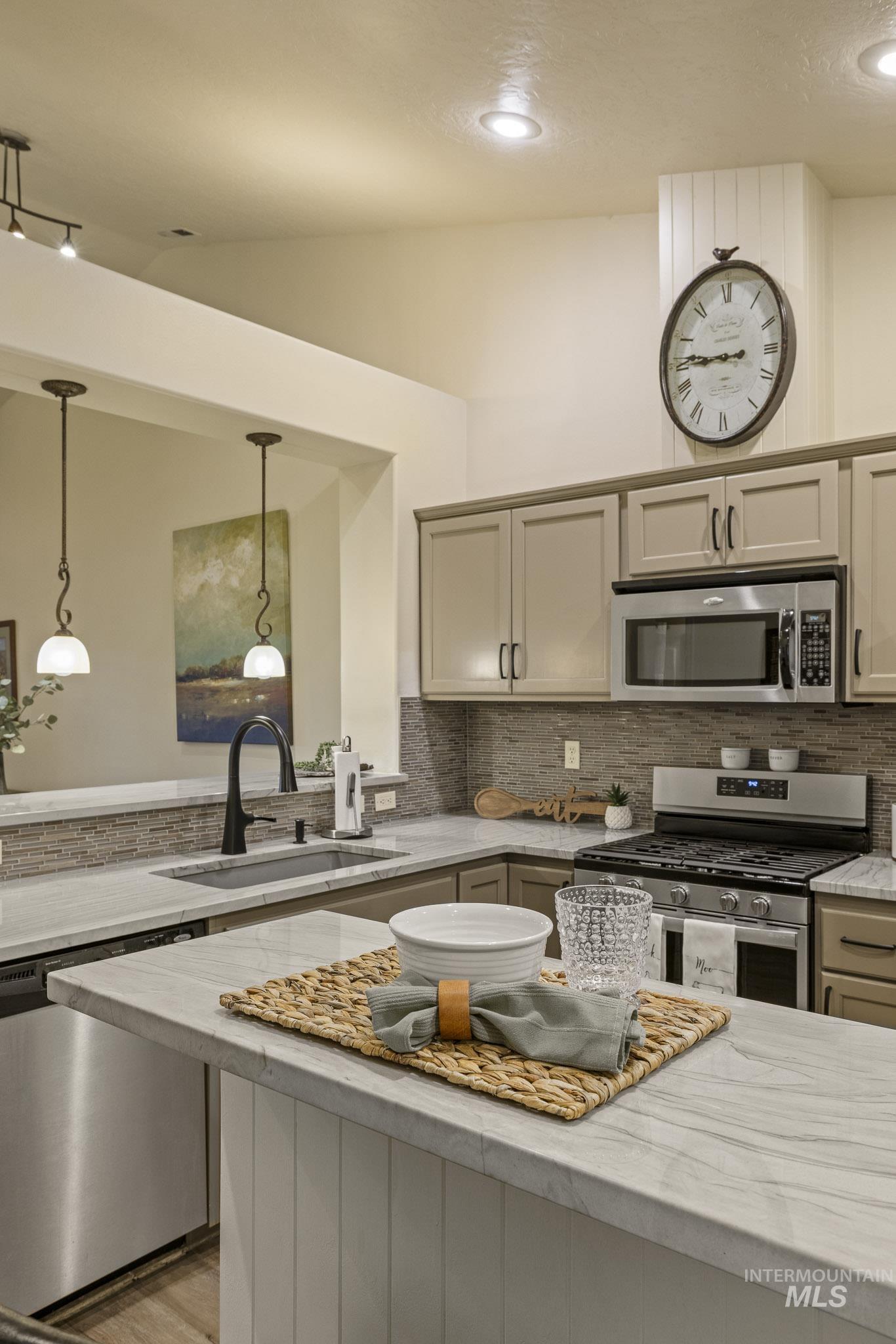 Kitchen featuring appliances with stainless steel finishes, light stone countertops, decorative backsplash, vaulted ceiling, and hanging light fixtures