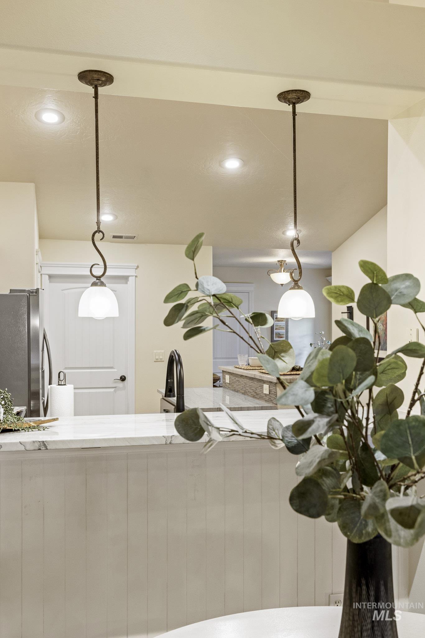 Kitchen featuring freestanding refrigerator, hanging light fixtures, light stone countertops, and recessed lighting