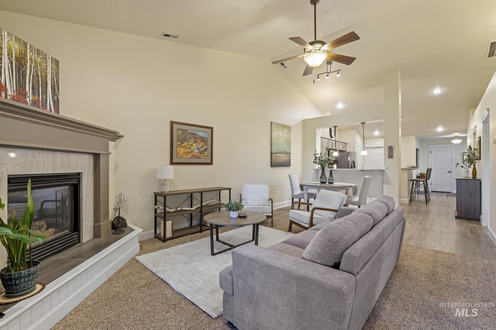 Living room featuring a tiled fireplace, ceiling fan, carpet floors, and high vaulted ceiling