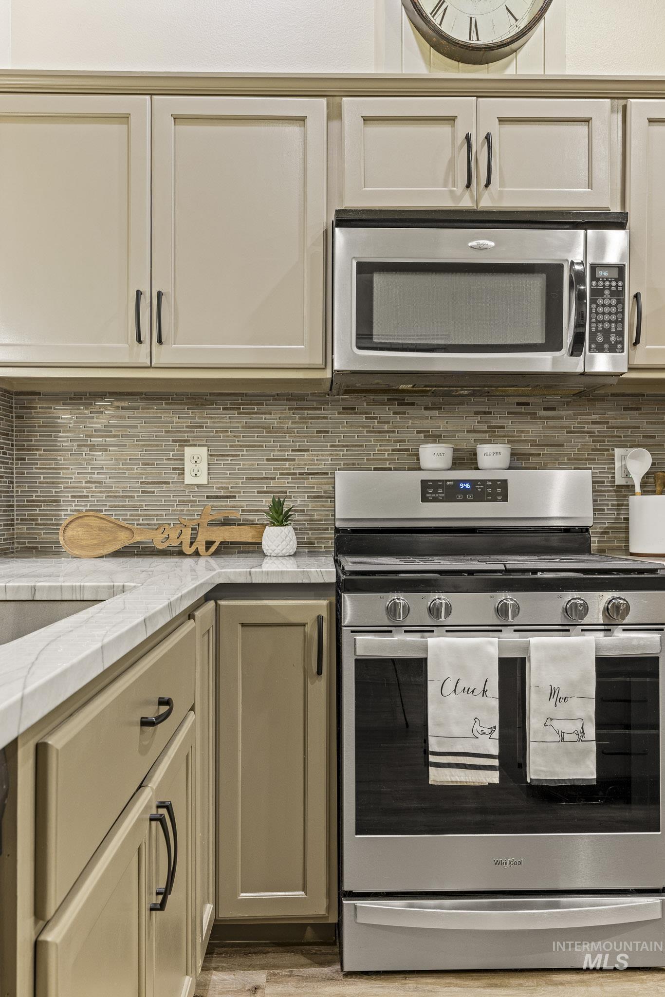 Kitchen with stainless steel appliances, decorative backsplash, and light stone countertops