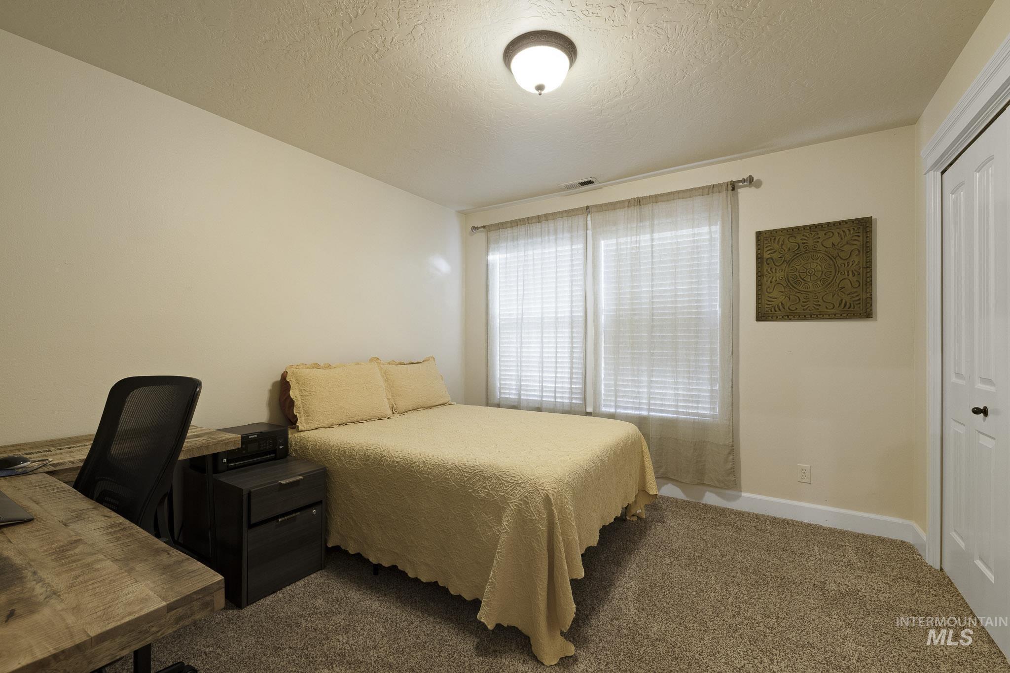 Carpeted bedroom featuring a textured ceiling, a closet, and an office area