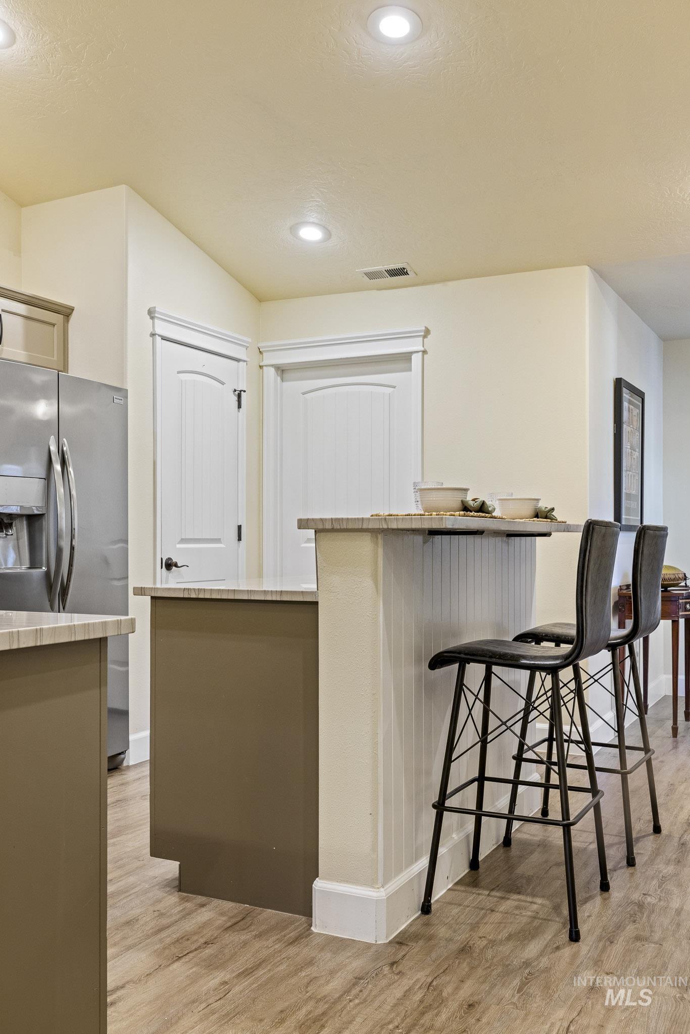 Kitchen with a breakfast bar area, light wood-style flooring, stainless steel fridge, recessed lighting, and light stone countertops