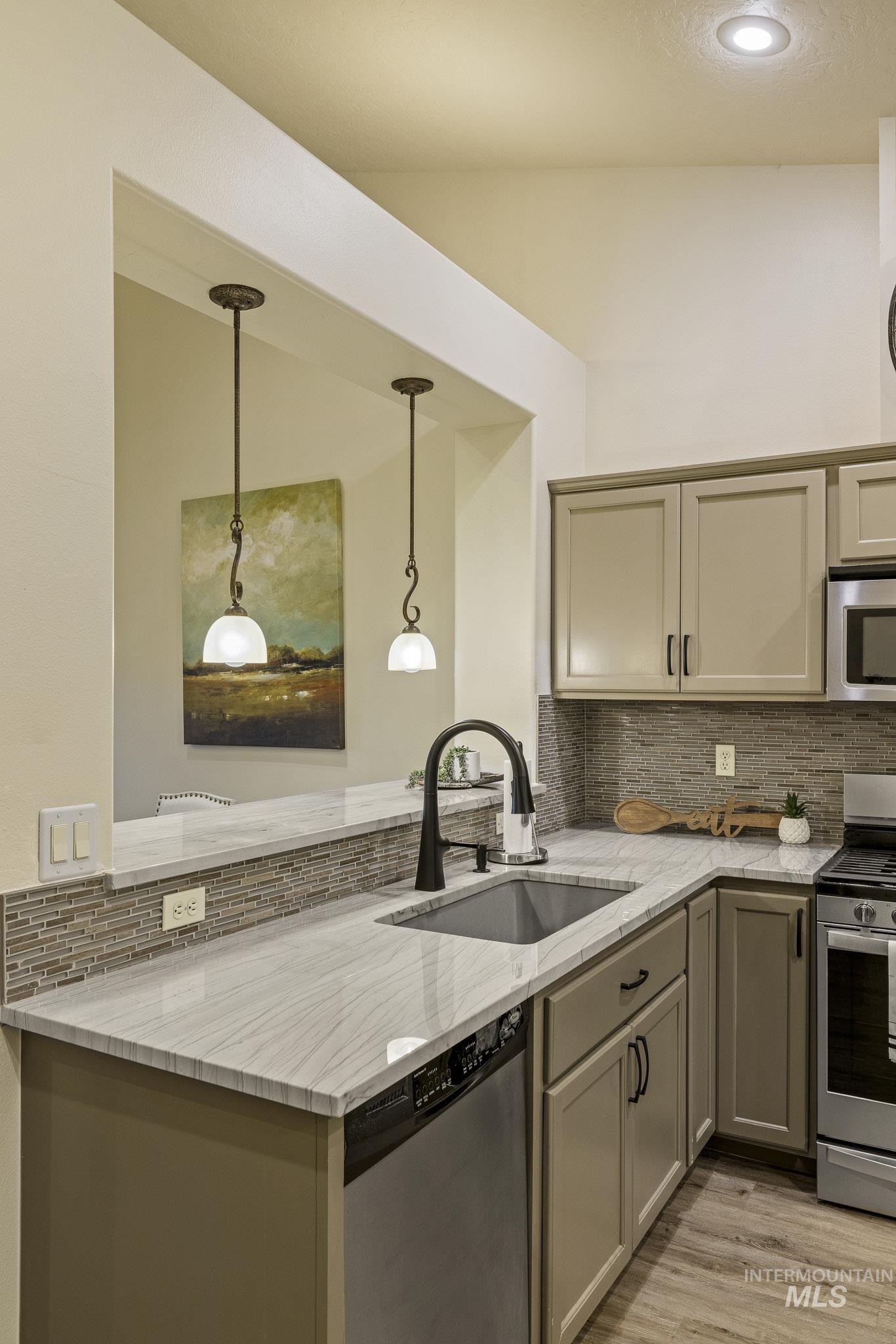 Kitchen with backsplash, gray cabinetry, light stone counters, stainless steel appliances, and pendant lighting