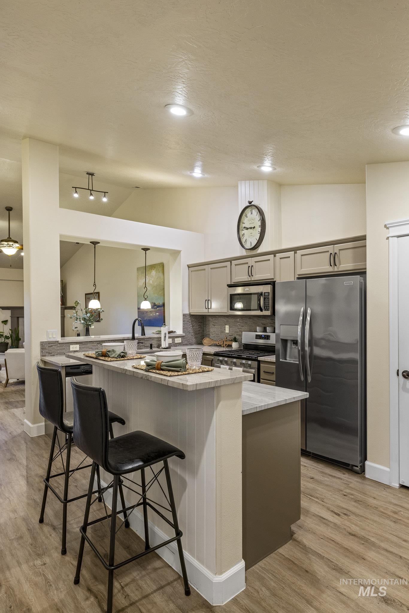 Kitchen featuring vaulted ceiling, a breakfast bar, a peninsula, backsplash, and stainless steel appliances