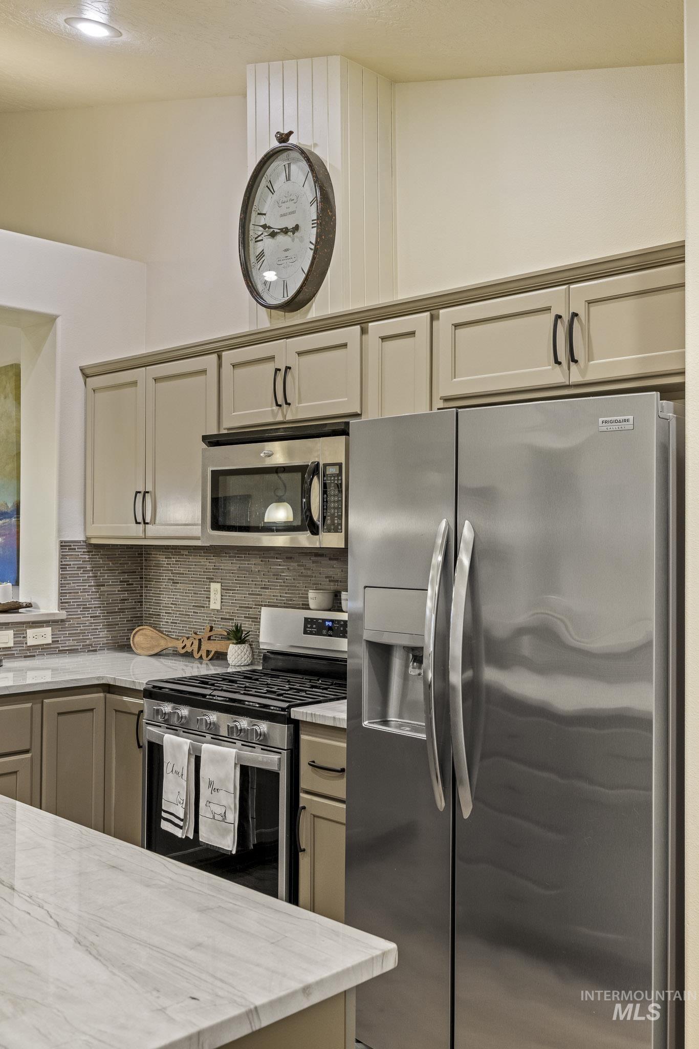 Kitchen featuring stainless steel appliances, light stone countertops, decorative backsplash, and cream cabinets