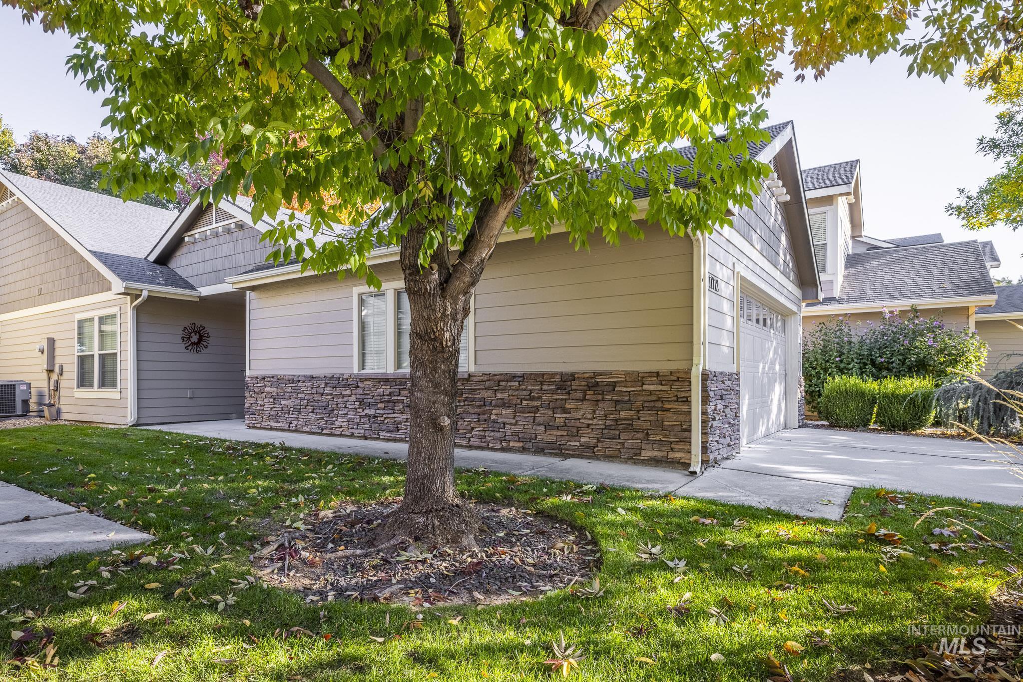 View of side of home with stone siding, a yard, an attached garage, and driveway