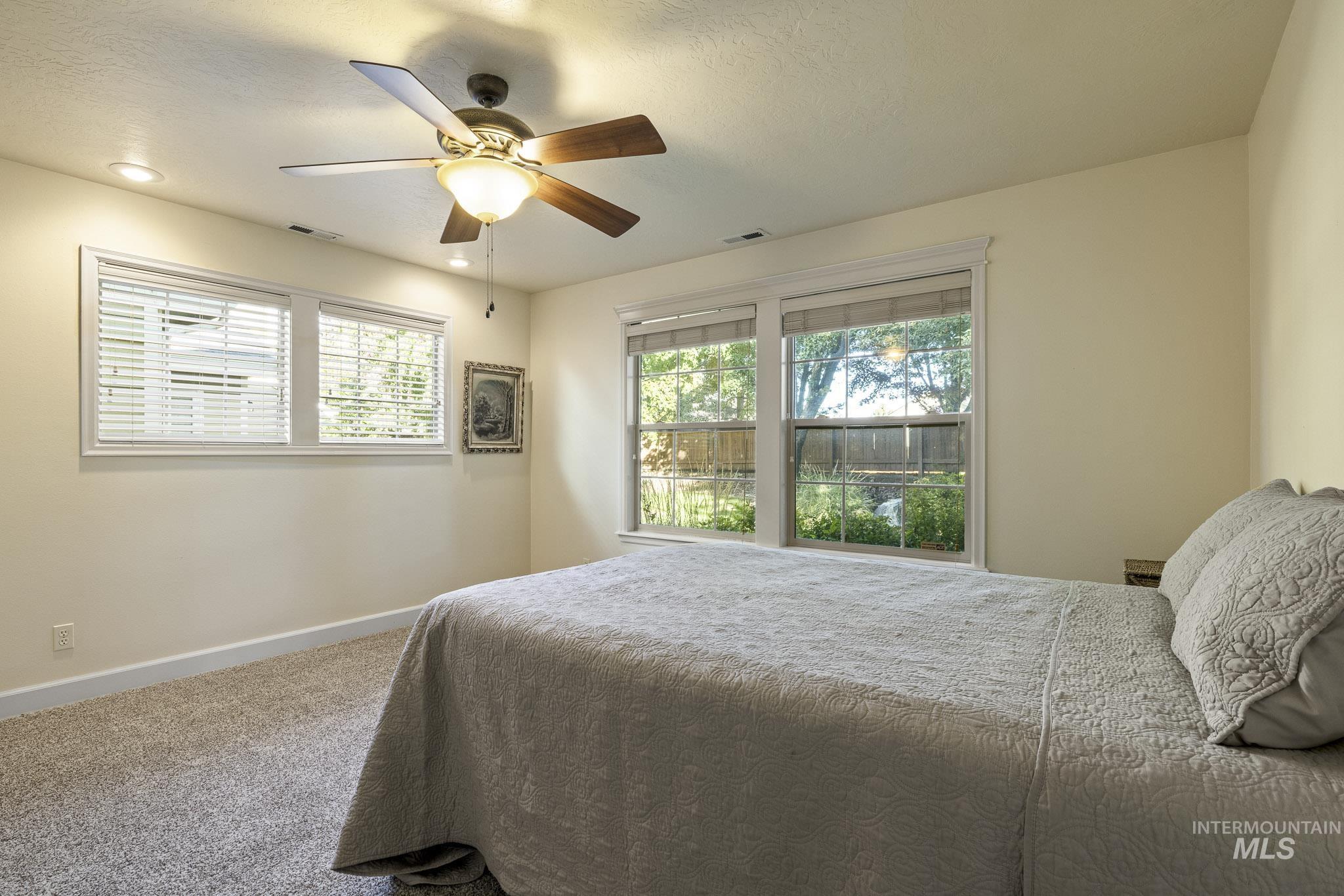 Carpeted bedroom with multiple windows, ceiling fan, and a textured ceiling