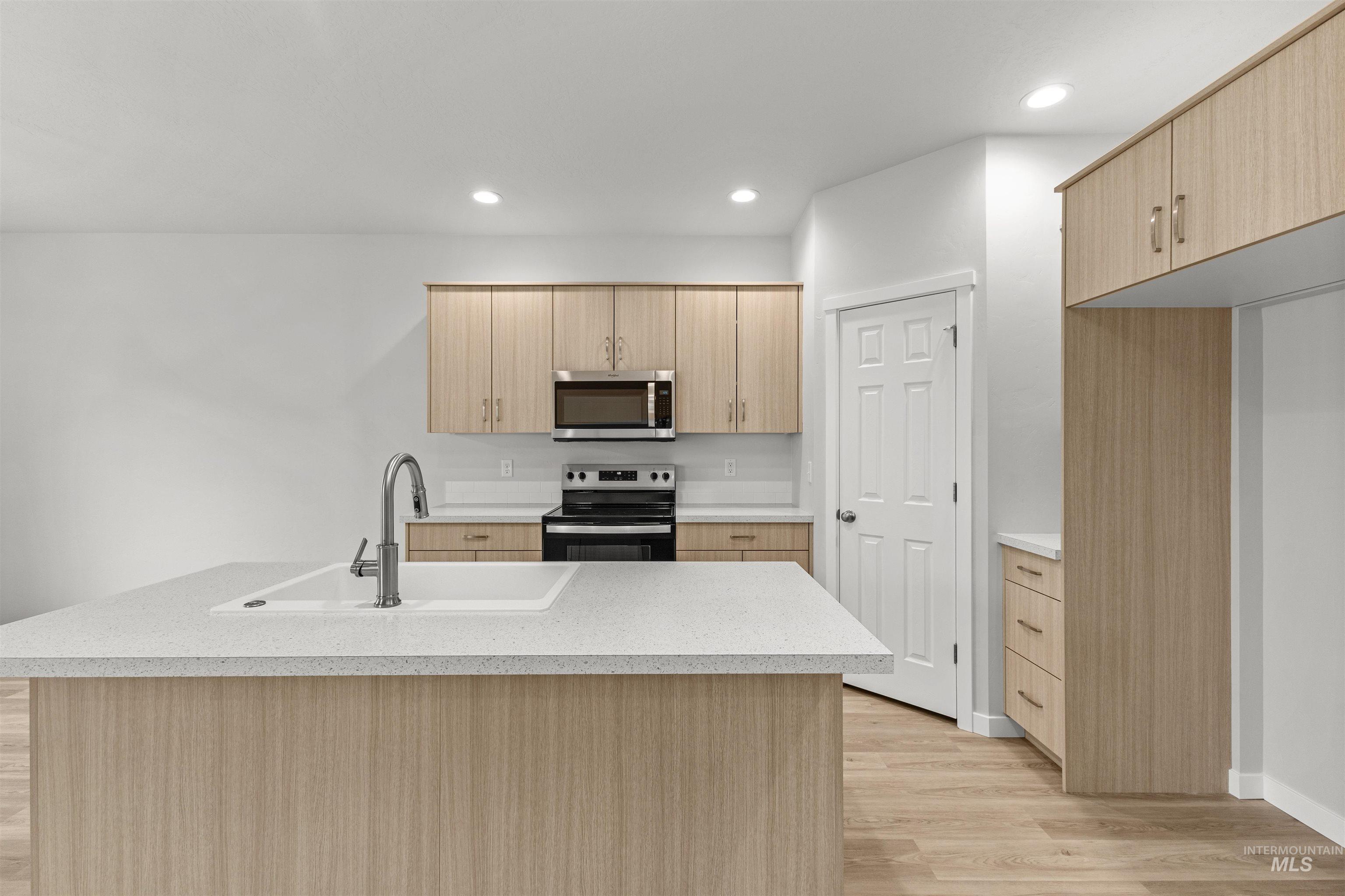 Kitchen featuring appliances with stainless steel finishes, a kitchen island with sink, light wood finished floors, light brown cabinetry, and recessed lighting
