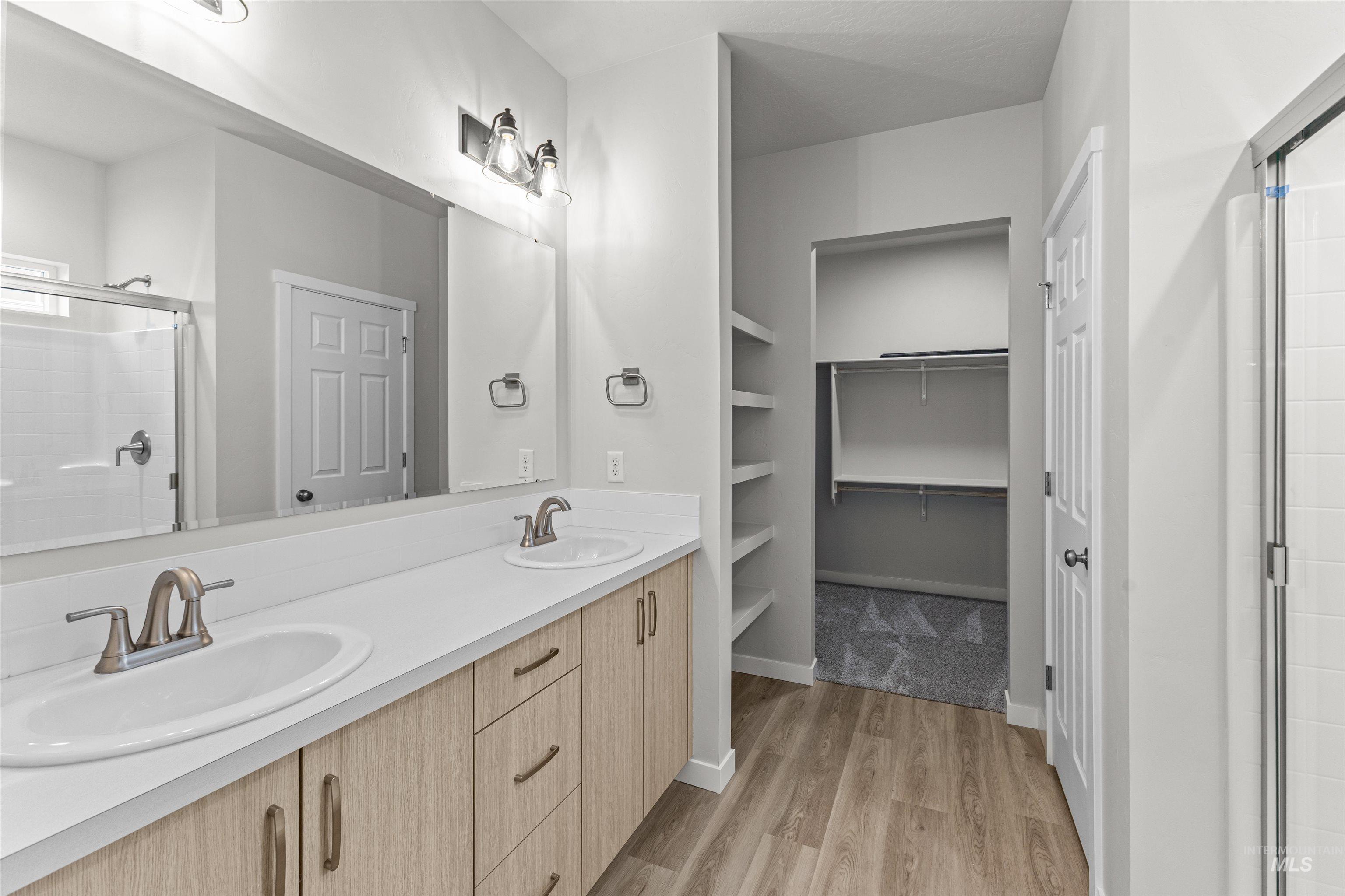 Full bathroom with a stall shower, double vanity, light wood-style flooring, and a spacious closet