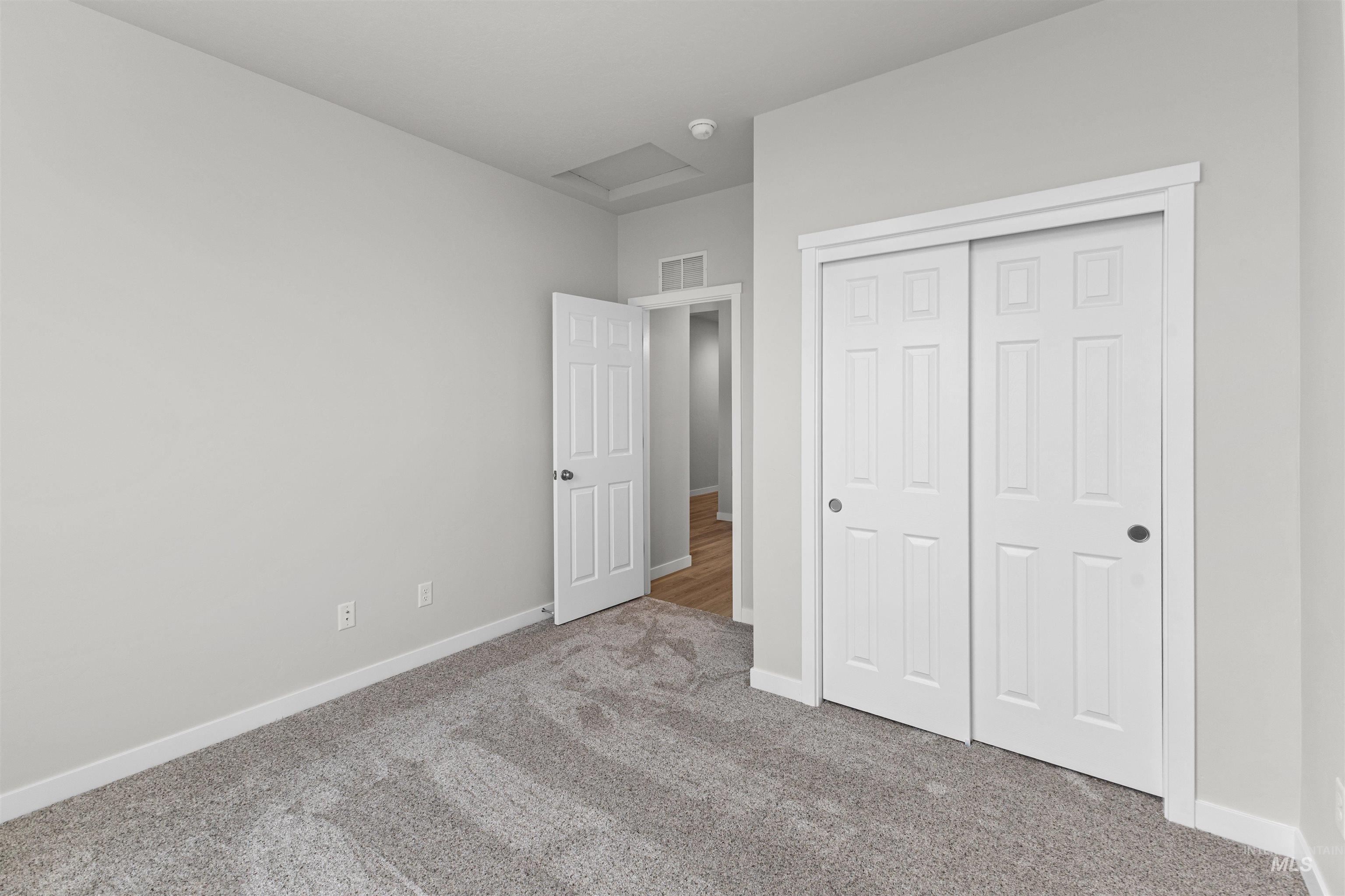 Unfurnished bedroom with attic access, carpet flooring, and a closet