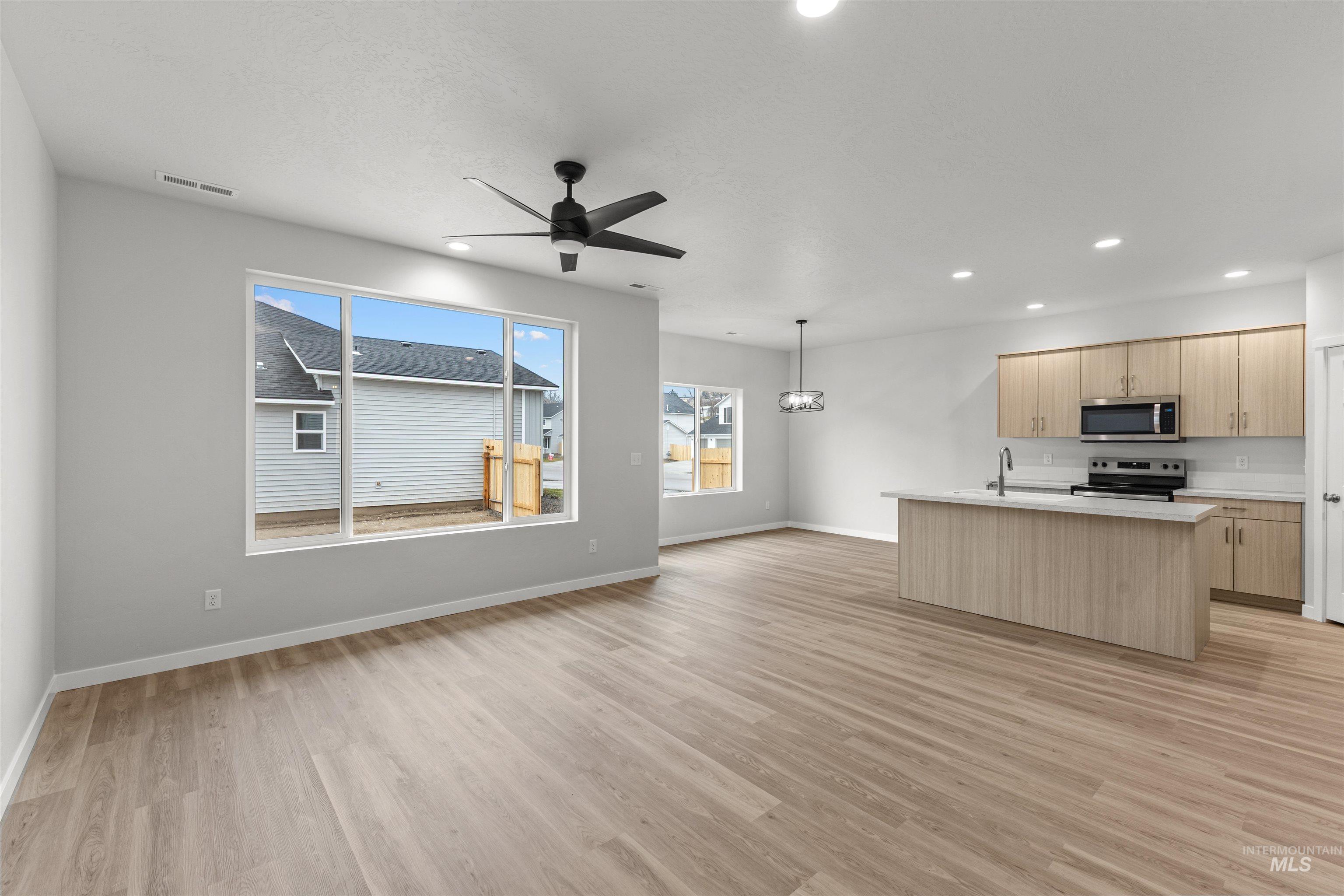 Kitchen featuring a center island with sink, light brown cabinets, stainless steel appliances, ceiling fan, and open floor plan