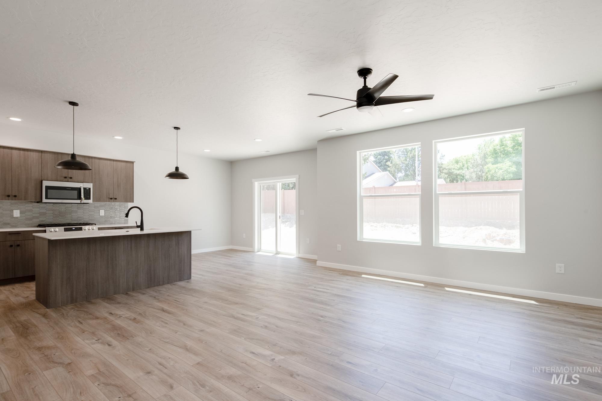 Kitchen featuring stainless steel microwave, open floor plan, a kitchen island with sink, tasteful backsplash, and light countertops