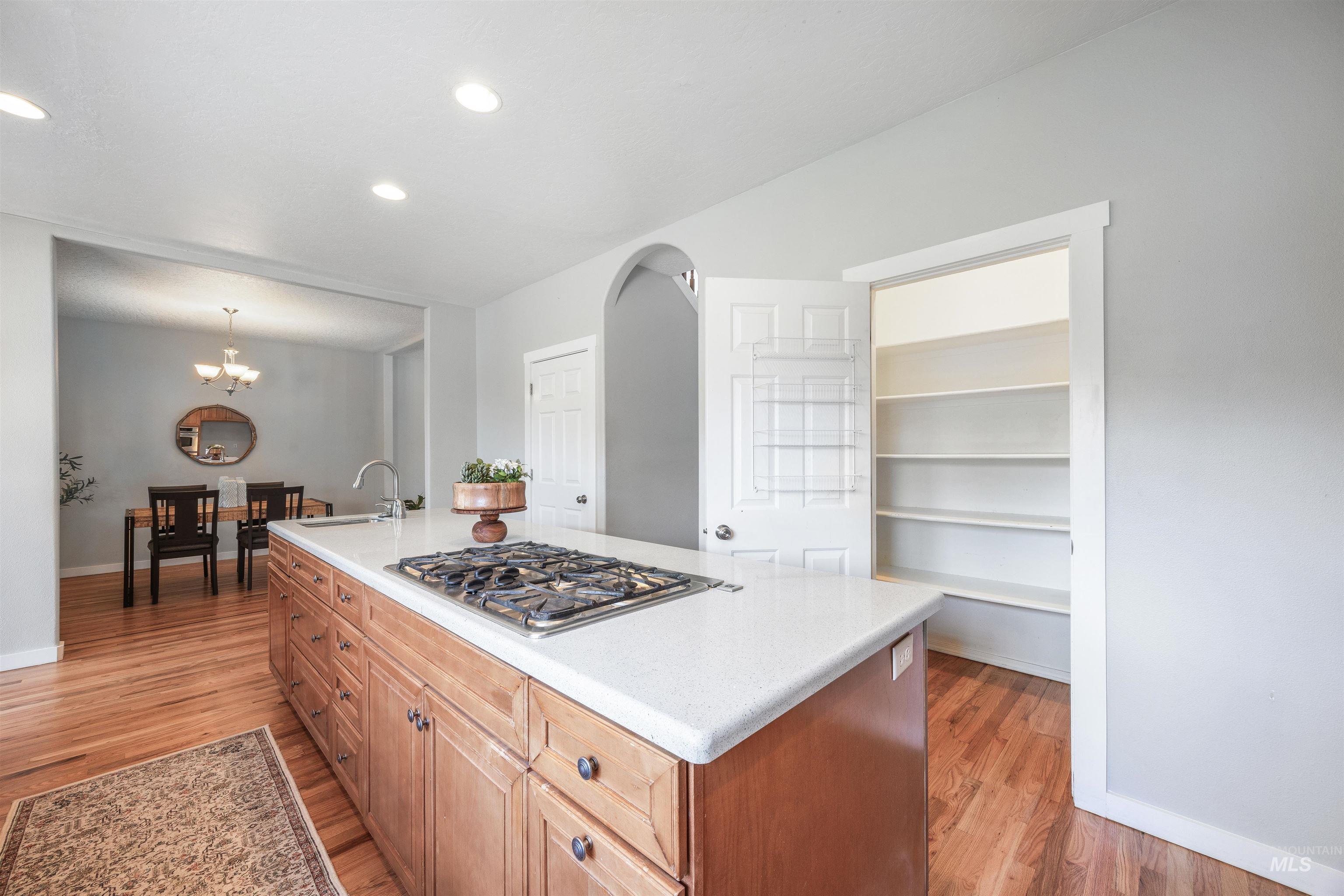 Kitchen with light wood finished floors, brown cabinetry, an island with sink, and recessed lighting