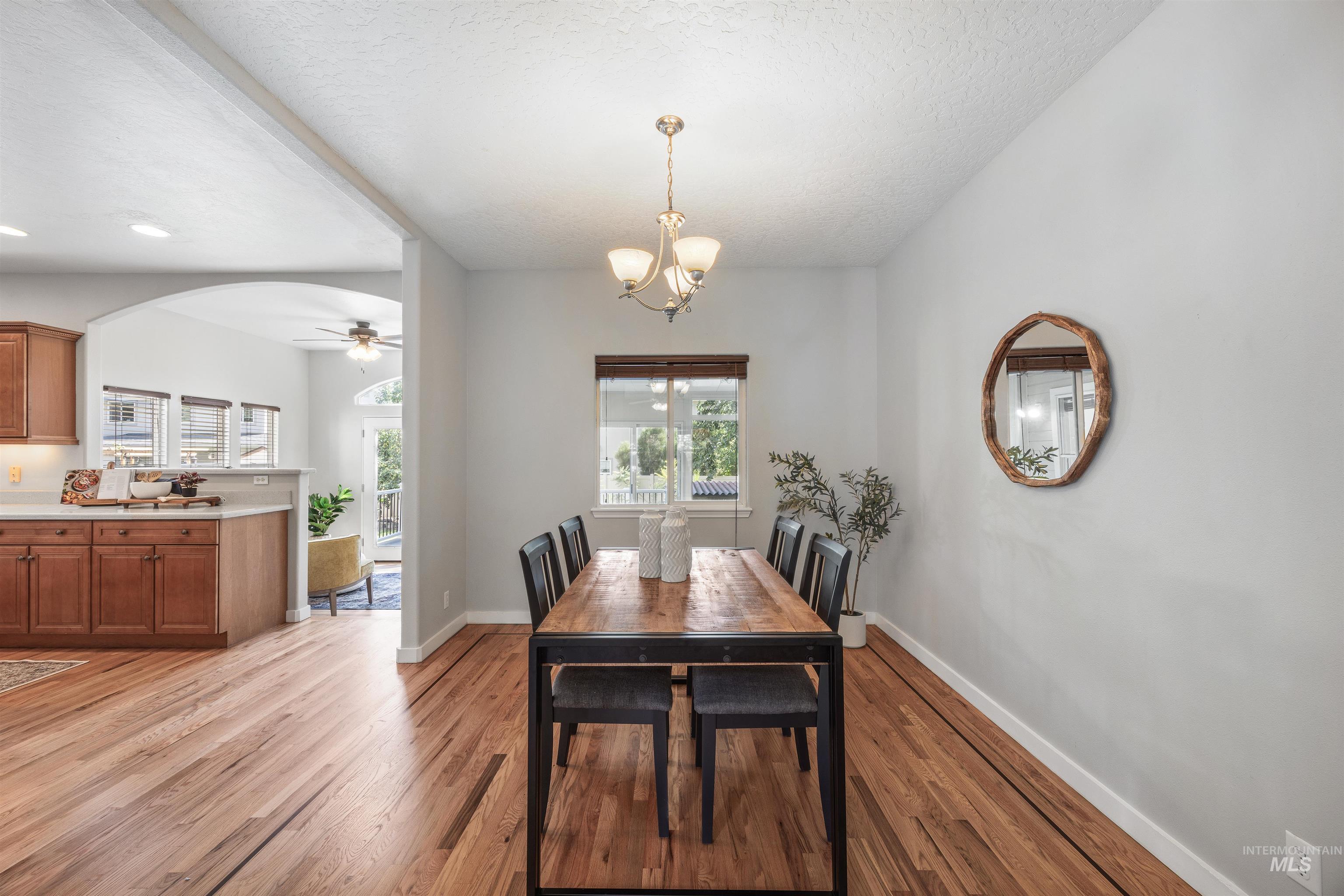 Dining space featuring light wood-style floors, arched walkways, a textured ceiling, a ceiling fan, and a chandelier
