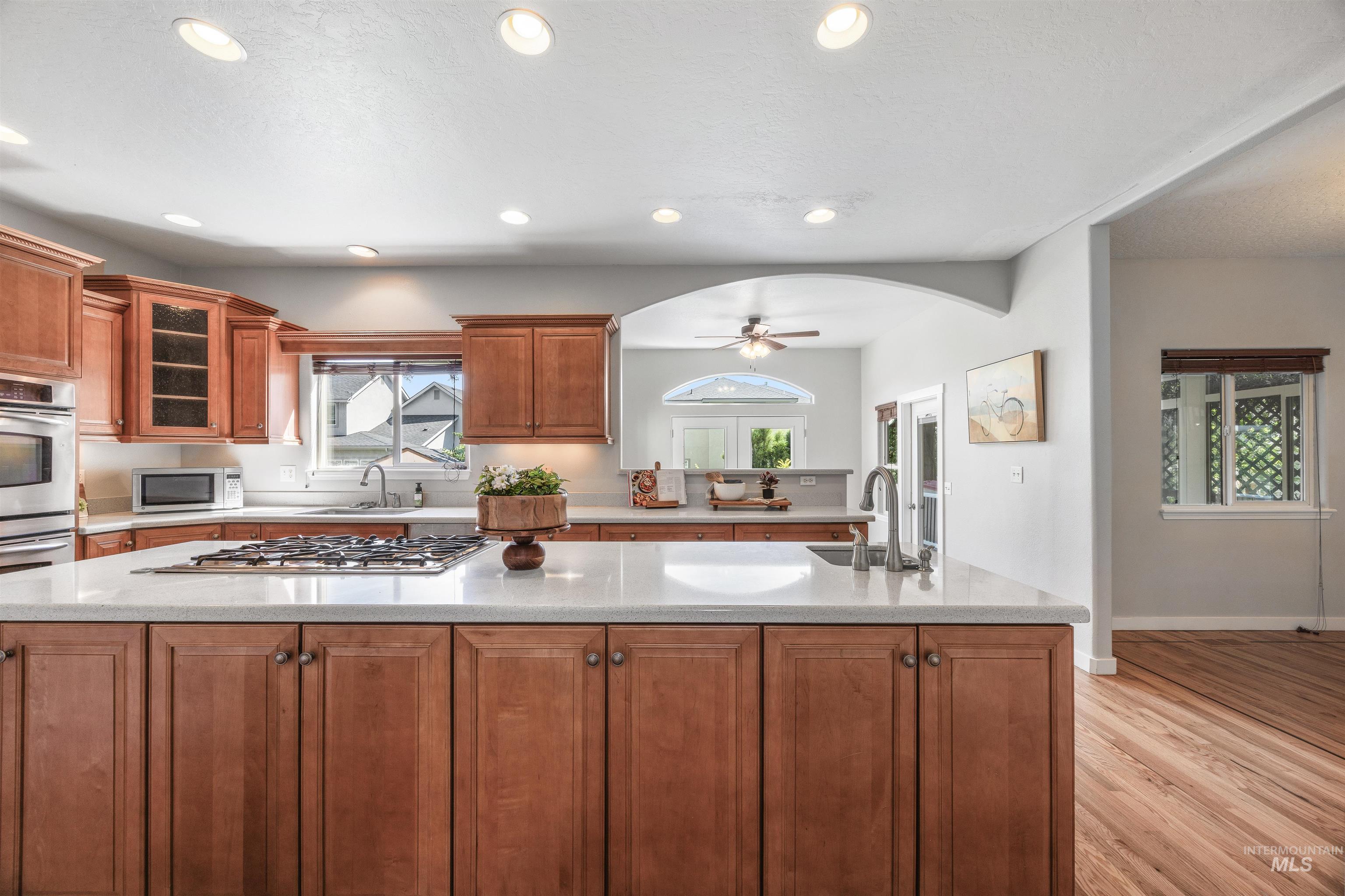 Kitchen with brown cabinets, light wood-style floors, ceiling fan, recessed lighting, and light stone countertops