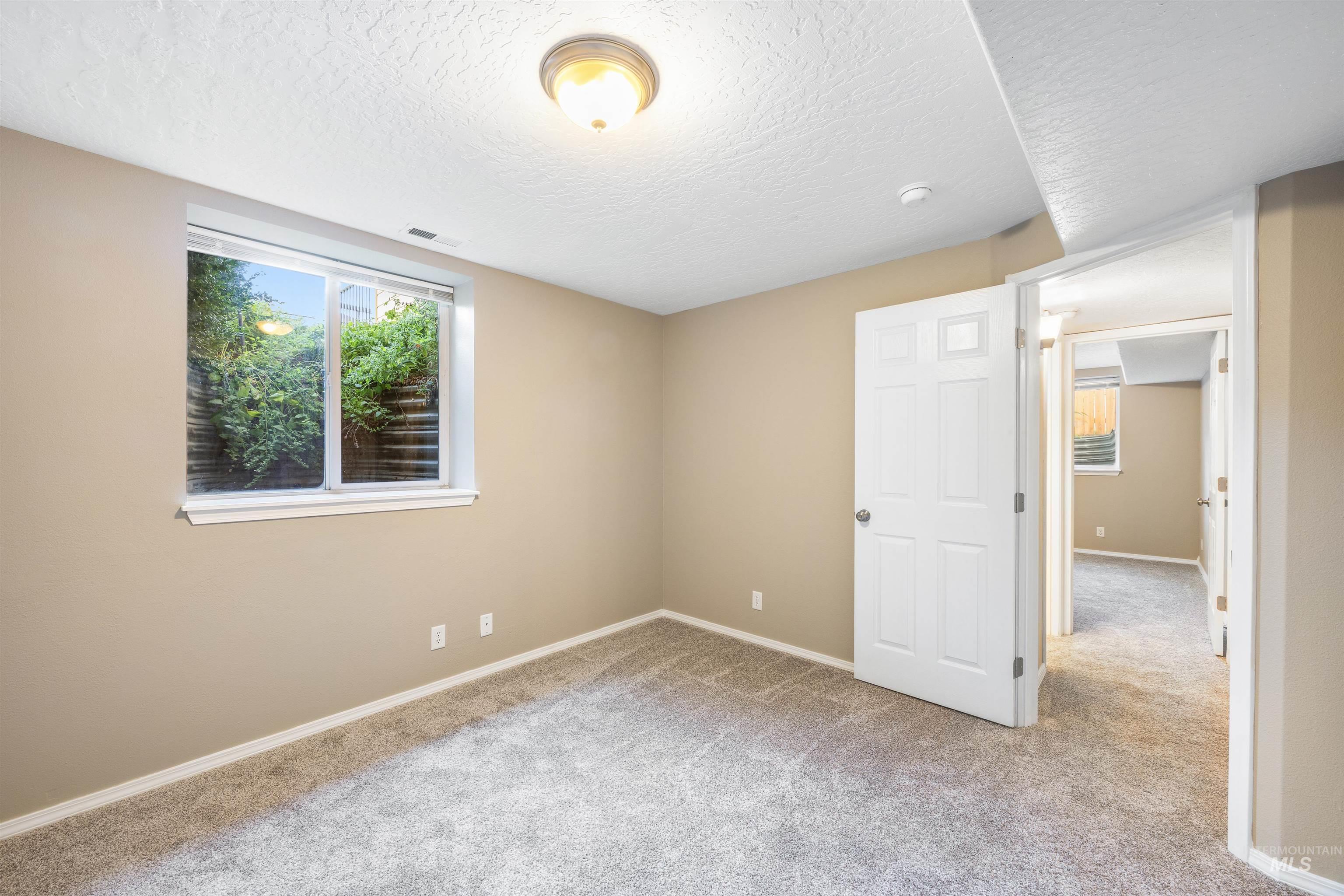 Unfurnished bedroom featuring light carpet, multiple windows, and a textured ceiling