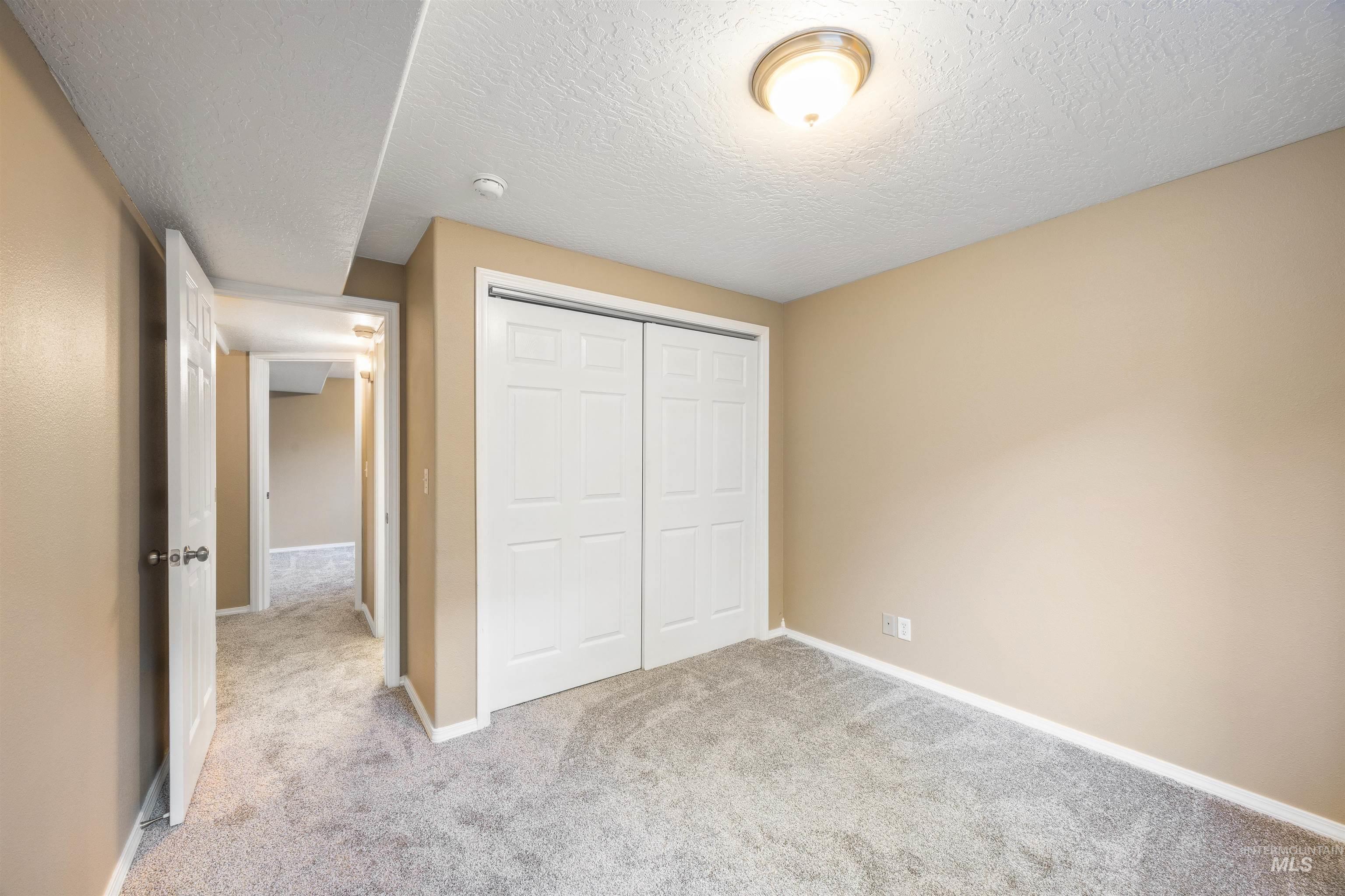 Unfurnished bedroom featuring a textured ceiling, light colored carpet, and a closet