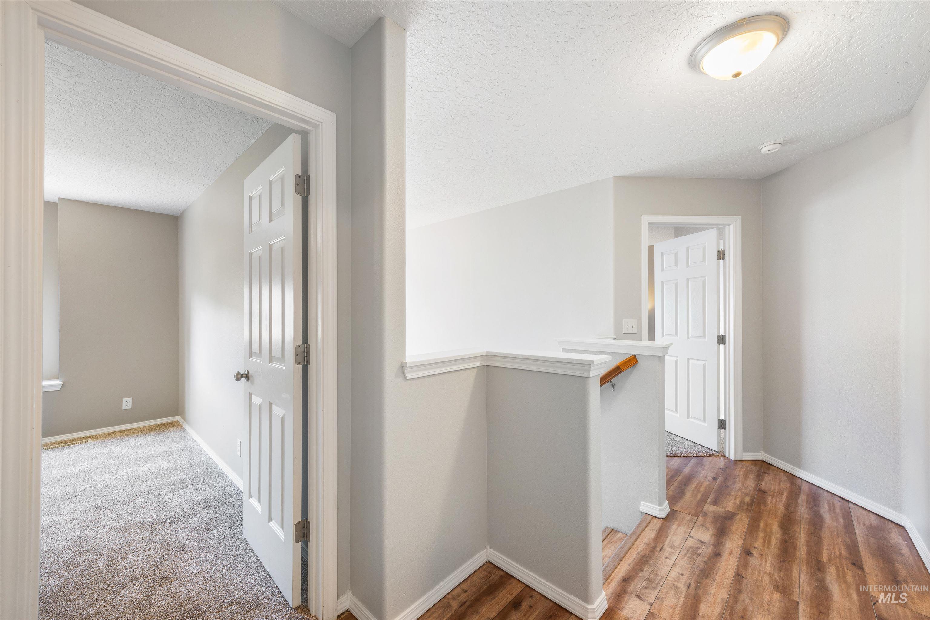 Hall with an upstairs landing, a textured ceiling, and wood finished floors