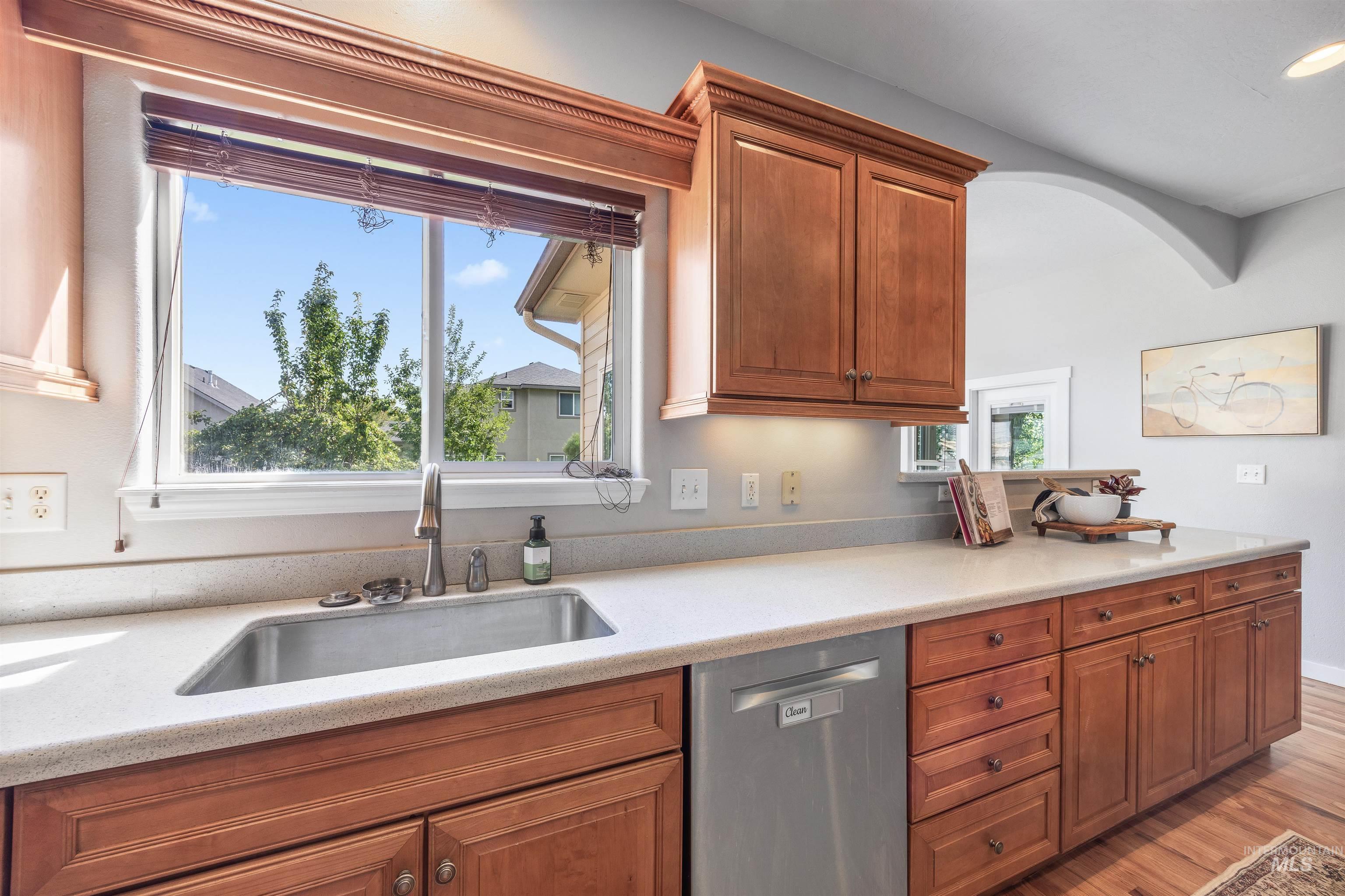 Kitchen featuring dishwasher, brown cabinets, light wood-style flooring, and light stone countertops