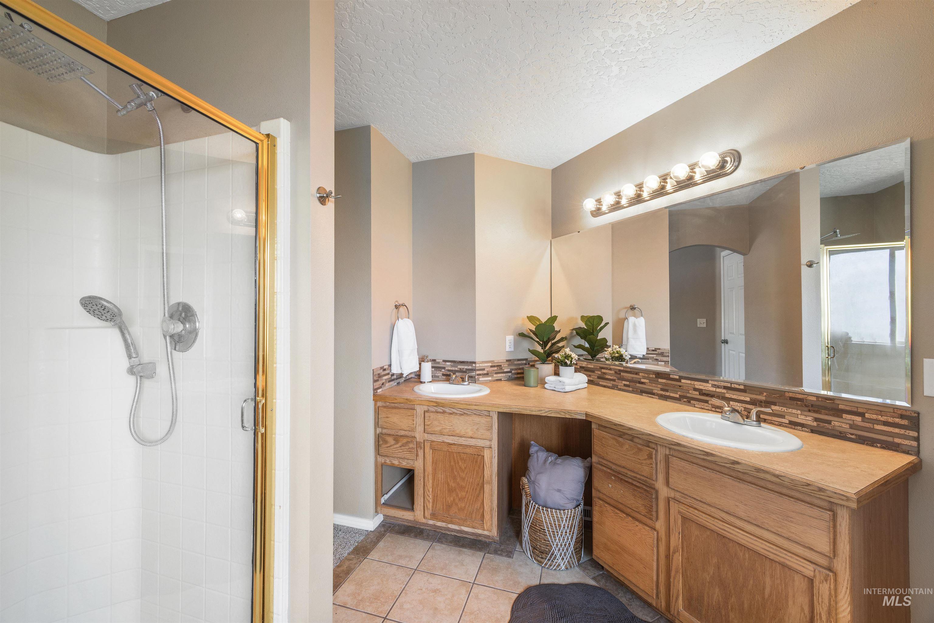 Bathroom with light tile patterned floors, double vanity, a shower stall, backsplash, and a textured ceiling