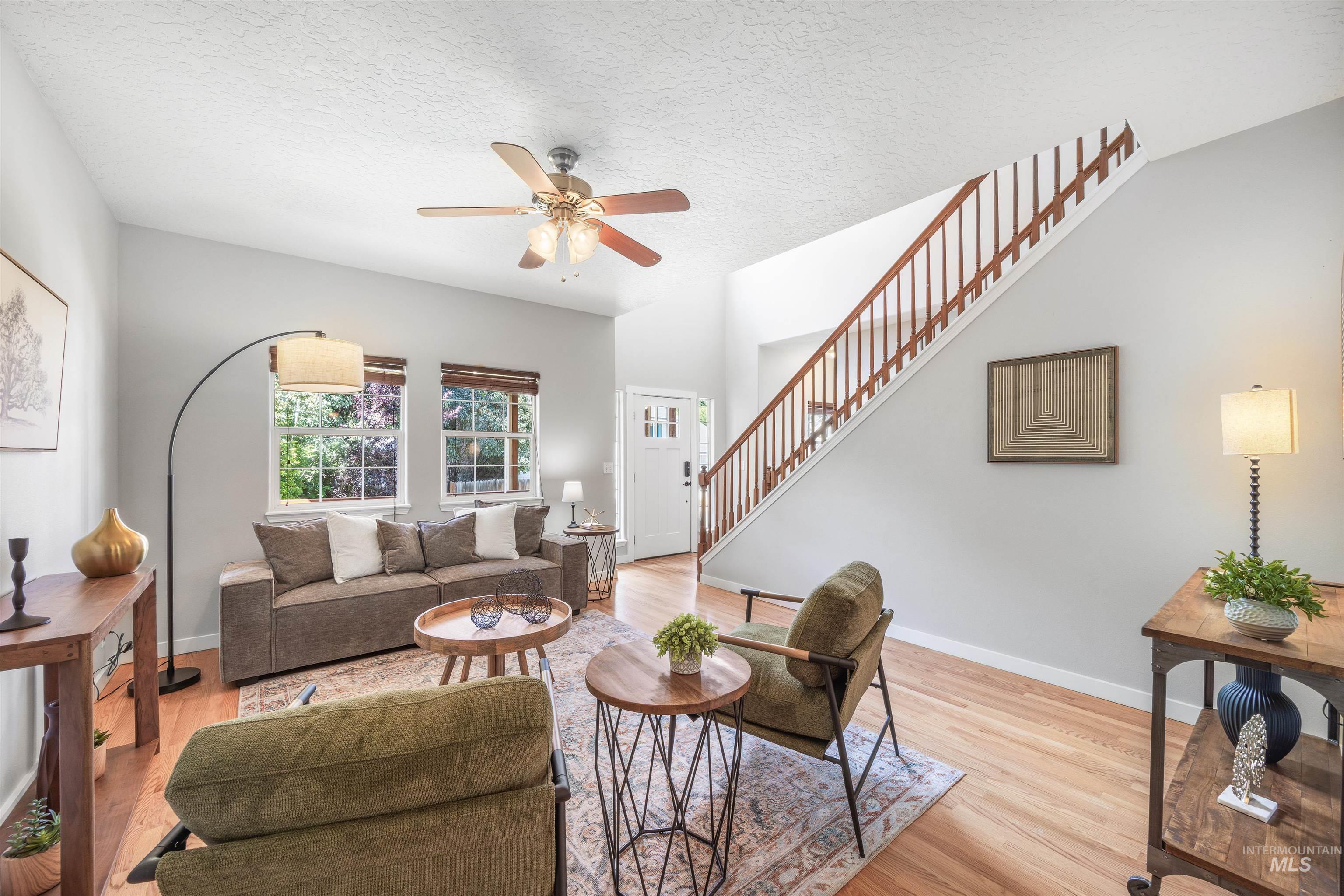 Living room with a textured ceiling, light wood-style flooring, ceiling fan, and stairs