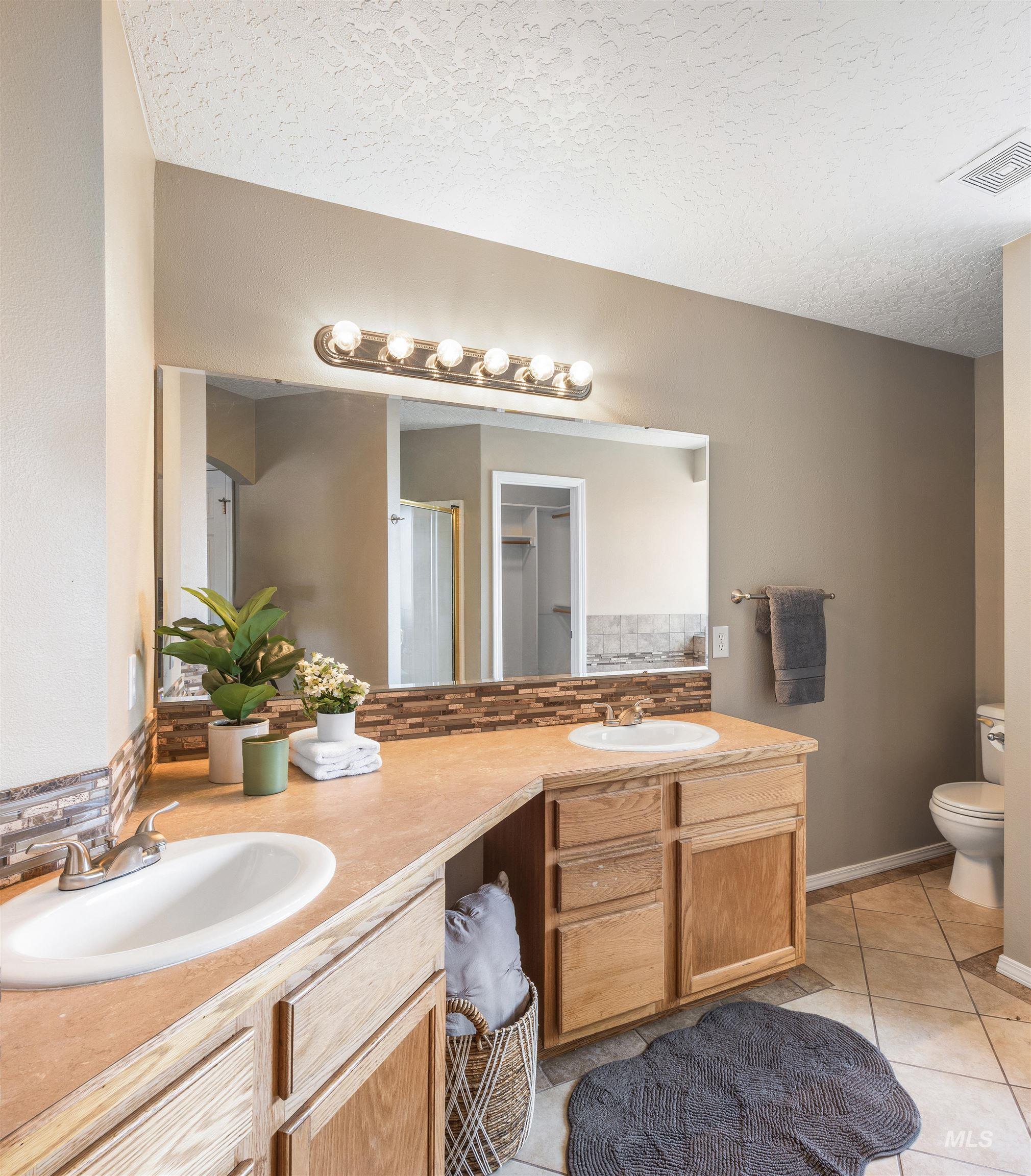 Full bathroom with double vanity, light tile patterned floors, a shower stall, a textured ceiling, and decorative backsplash