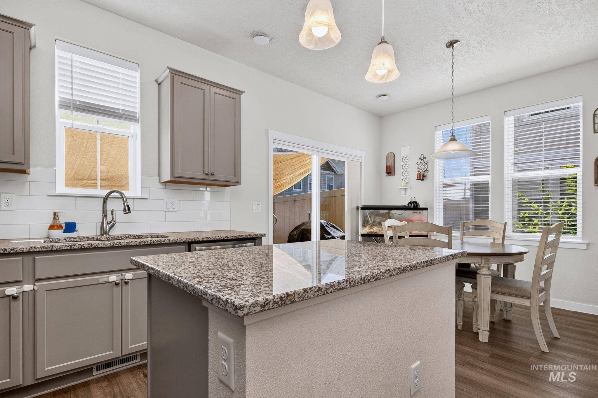 Kitchen featuring gray cabinetry, granite countertops, white subway tile backsplash, and wood-finish flooring