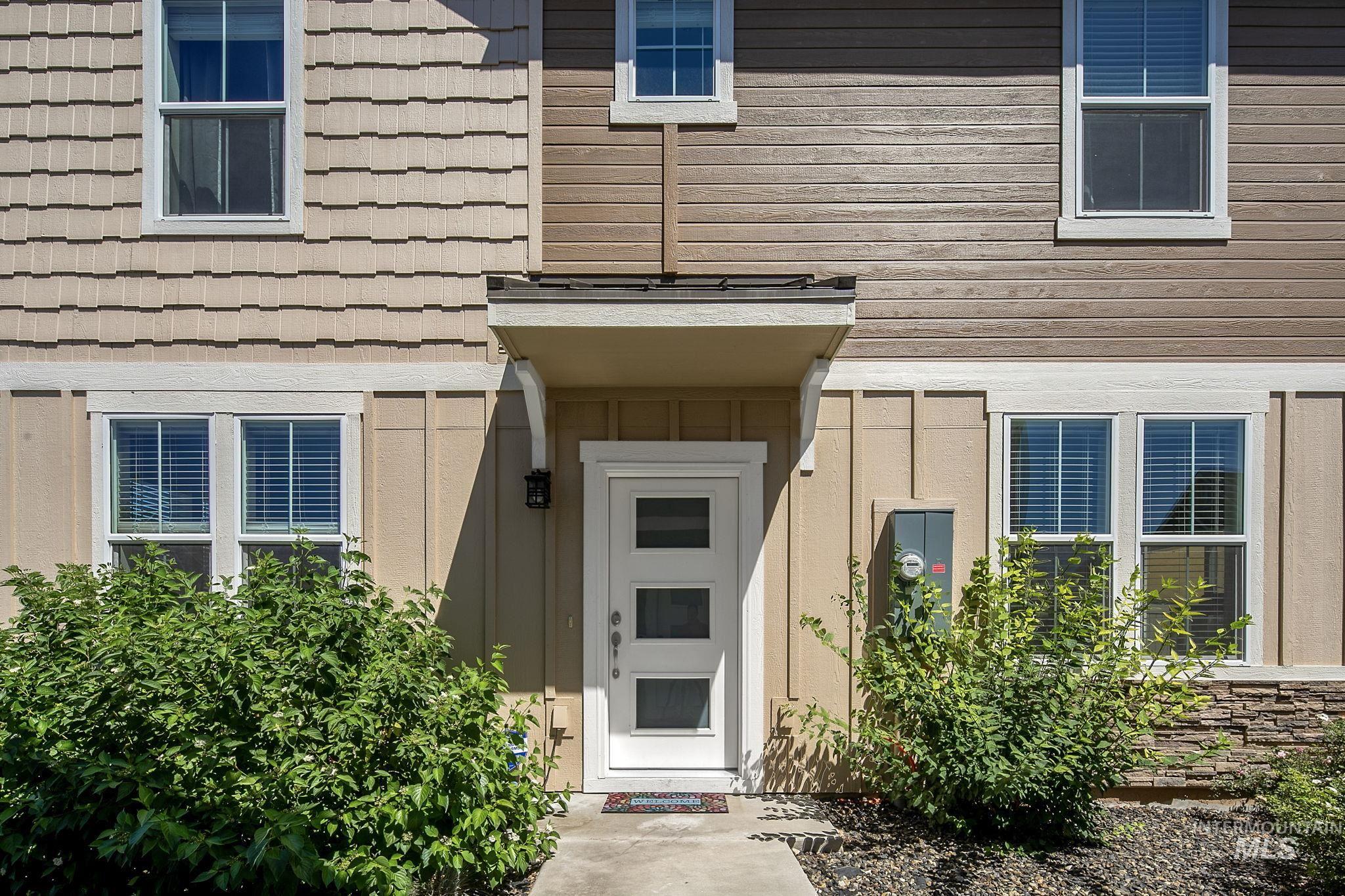 Modern fa?ade featuring a paneled entry door with frosted glass inserts, a covered porch, and white-framed windows with blinds