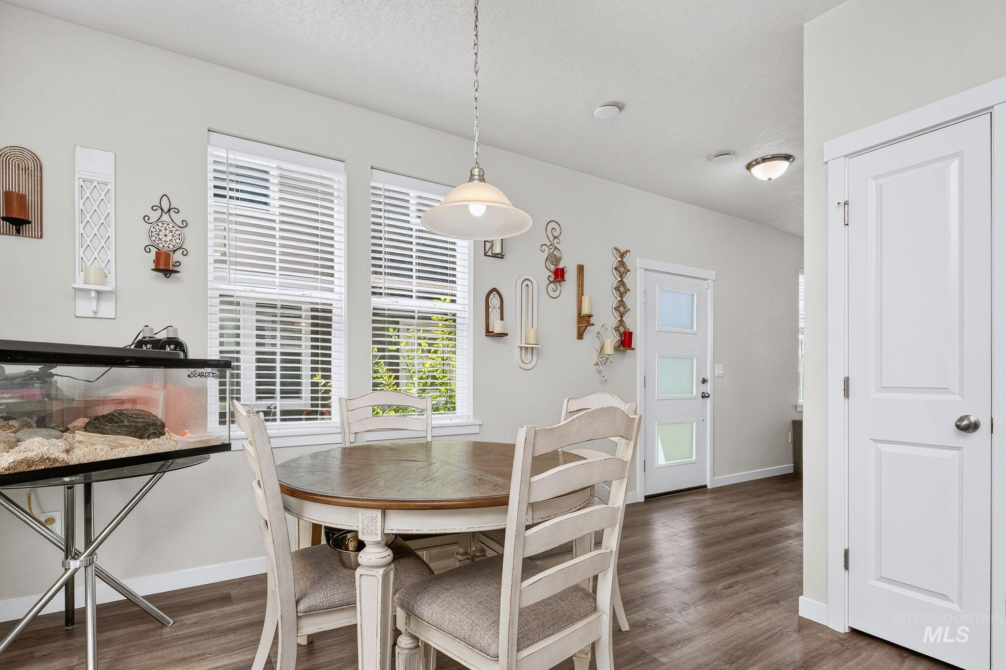 Light-filled interior space featuring two windows with blinds, wood-finish flooring, a white paneled door, and a white entry door with frosted glass panels