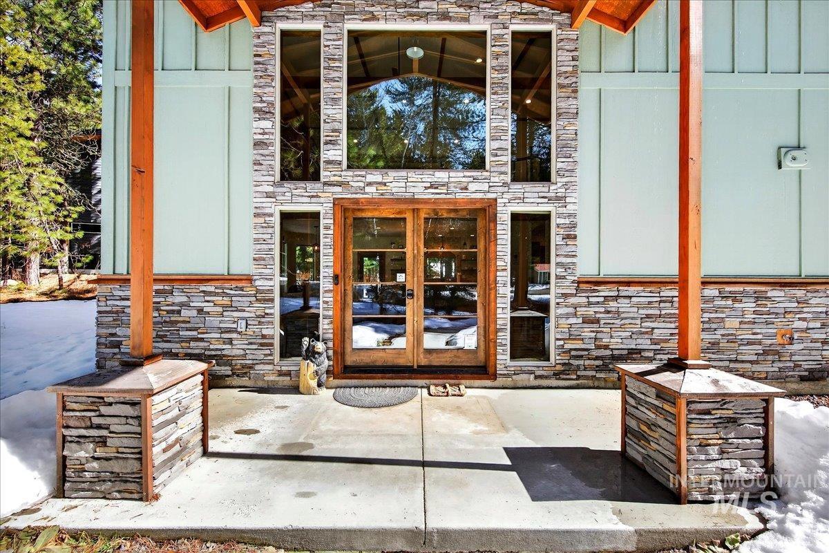 Doorway to property featuring board and batten siding, stone accent, french doors, and a patio