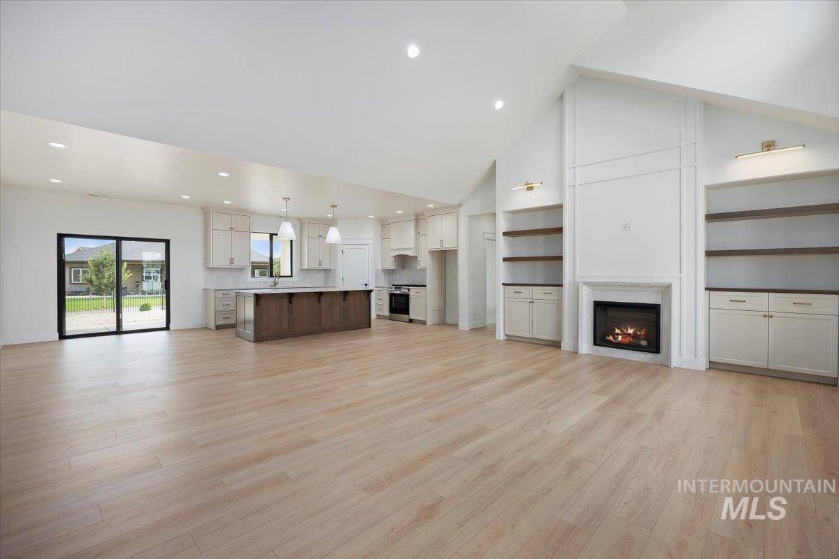 Unfurnished living room with recessed lighting, a lit fireplace, light wood-type flooring, and high vaulted ceiling