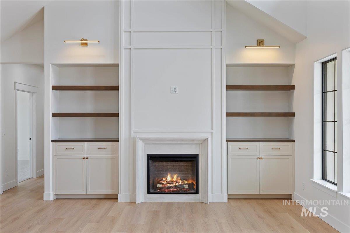 Unfurnished living room with a lit fireplace, built in shelves, and light wood finished floors