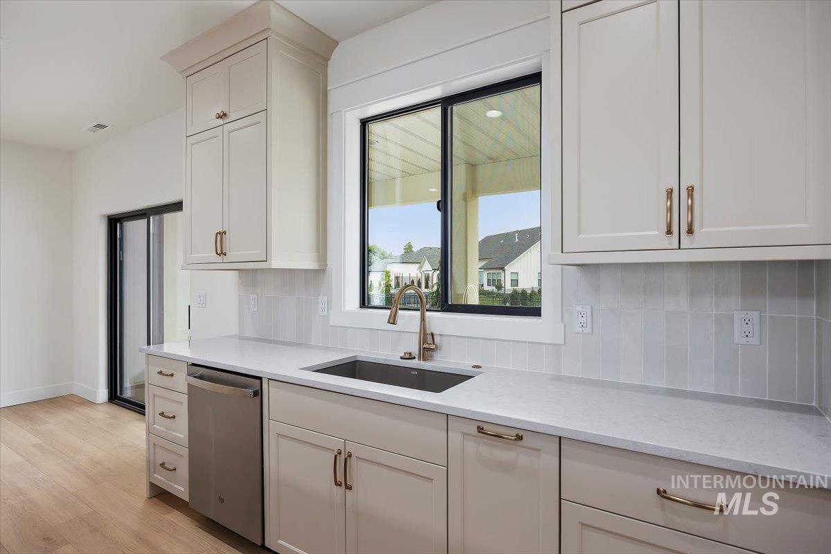 Kitchen featuring decorative backsplash, light stone countertops, stainless steel dishwasher, light wood finished floors, and white cabinetry