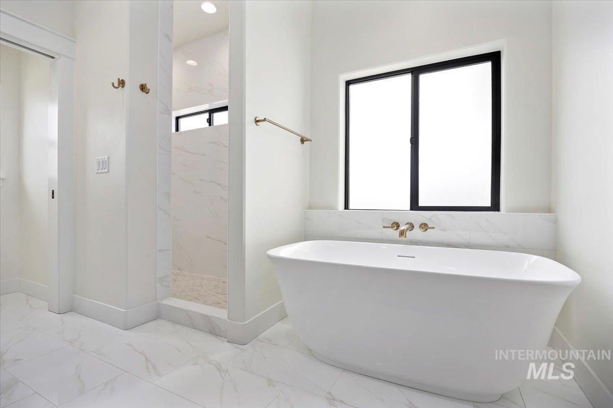Bathroom featuring light marble finish floors, a freestanding tub, and a marble finish shower
