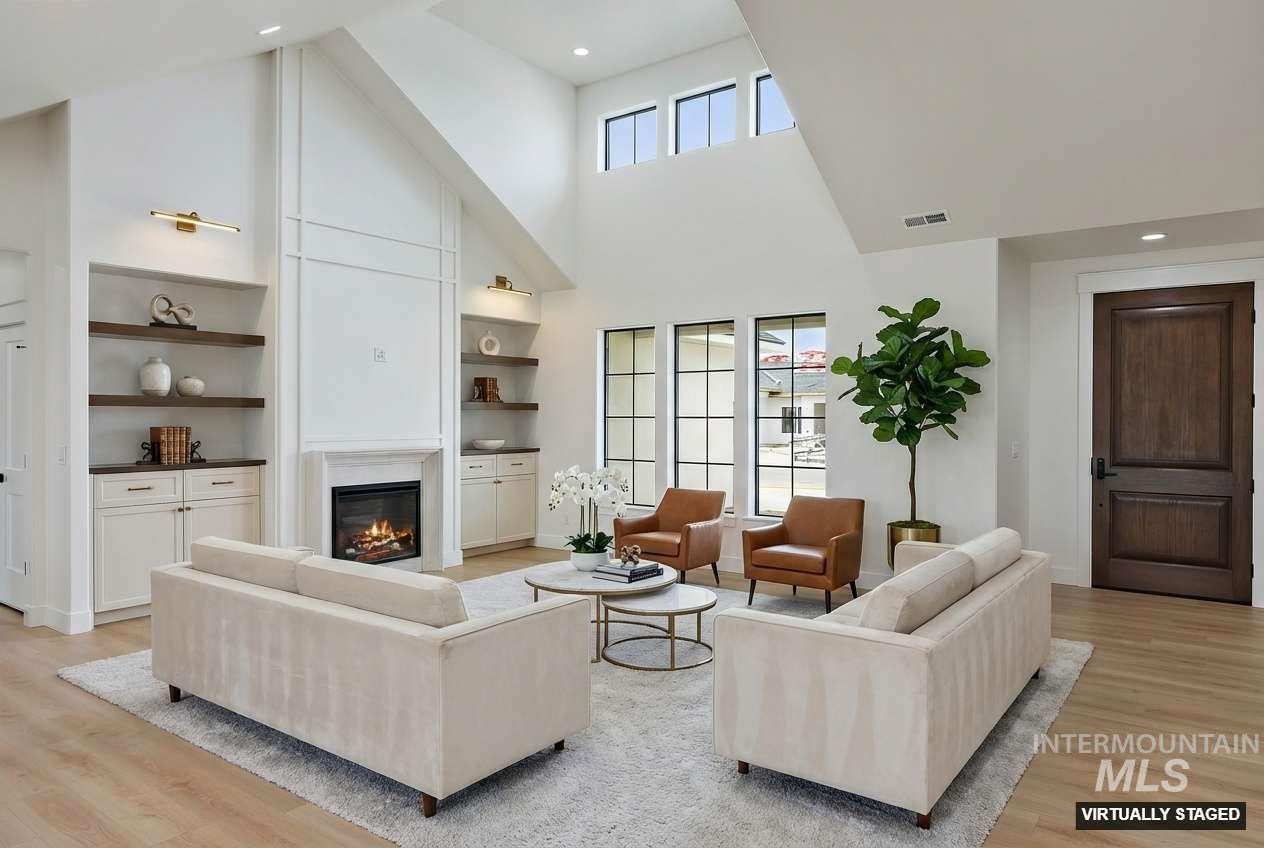 Living room with high vaulted ceiling, light wood finished floors, a glass covered fireplace, healthy amount of natural light, and recessed lighting