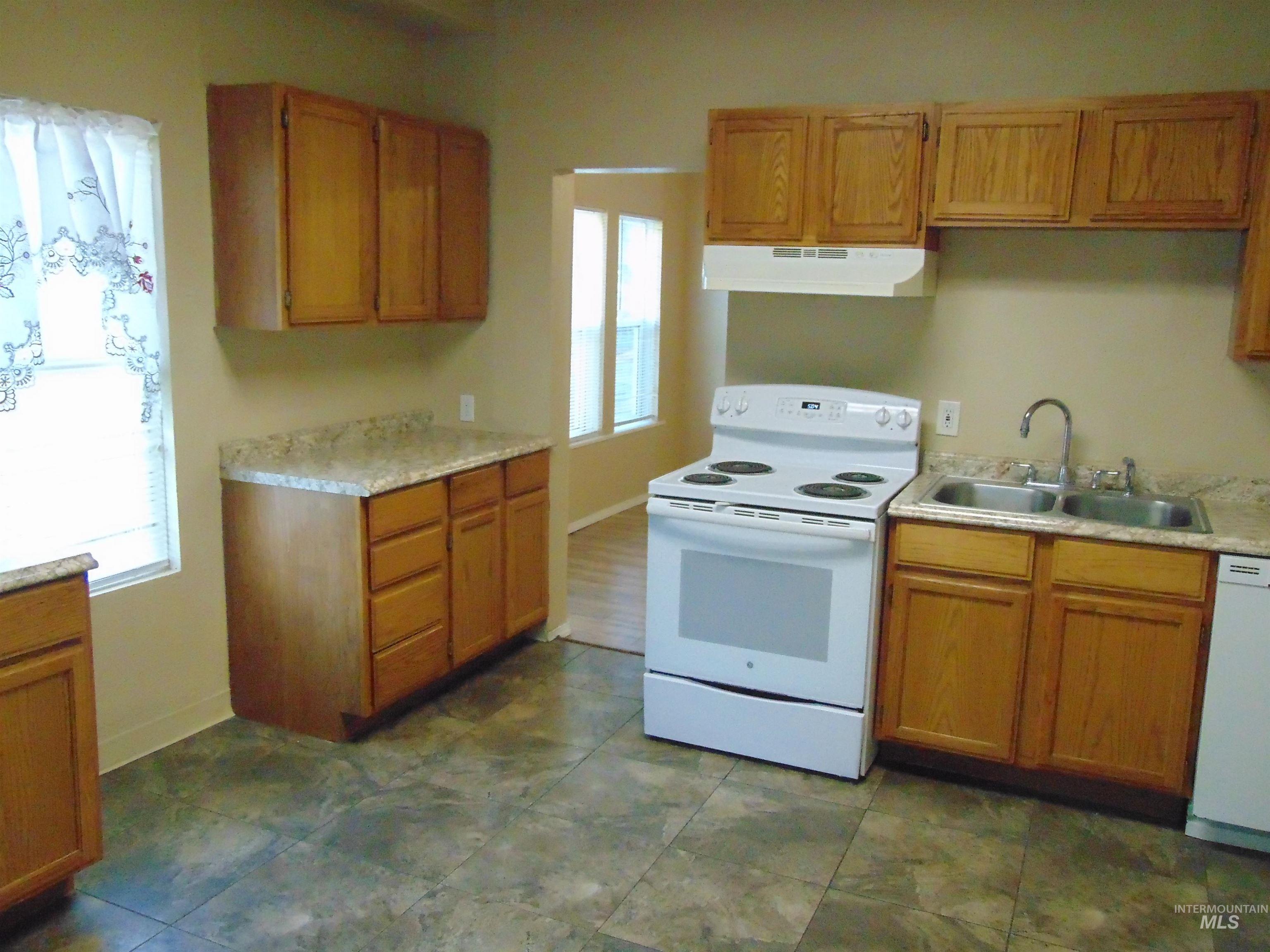 Kitchen with white appliances, light countertops, under cabinet range hood, and brown cabinets