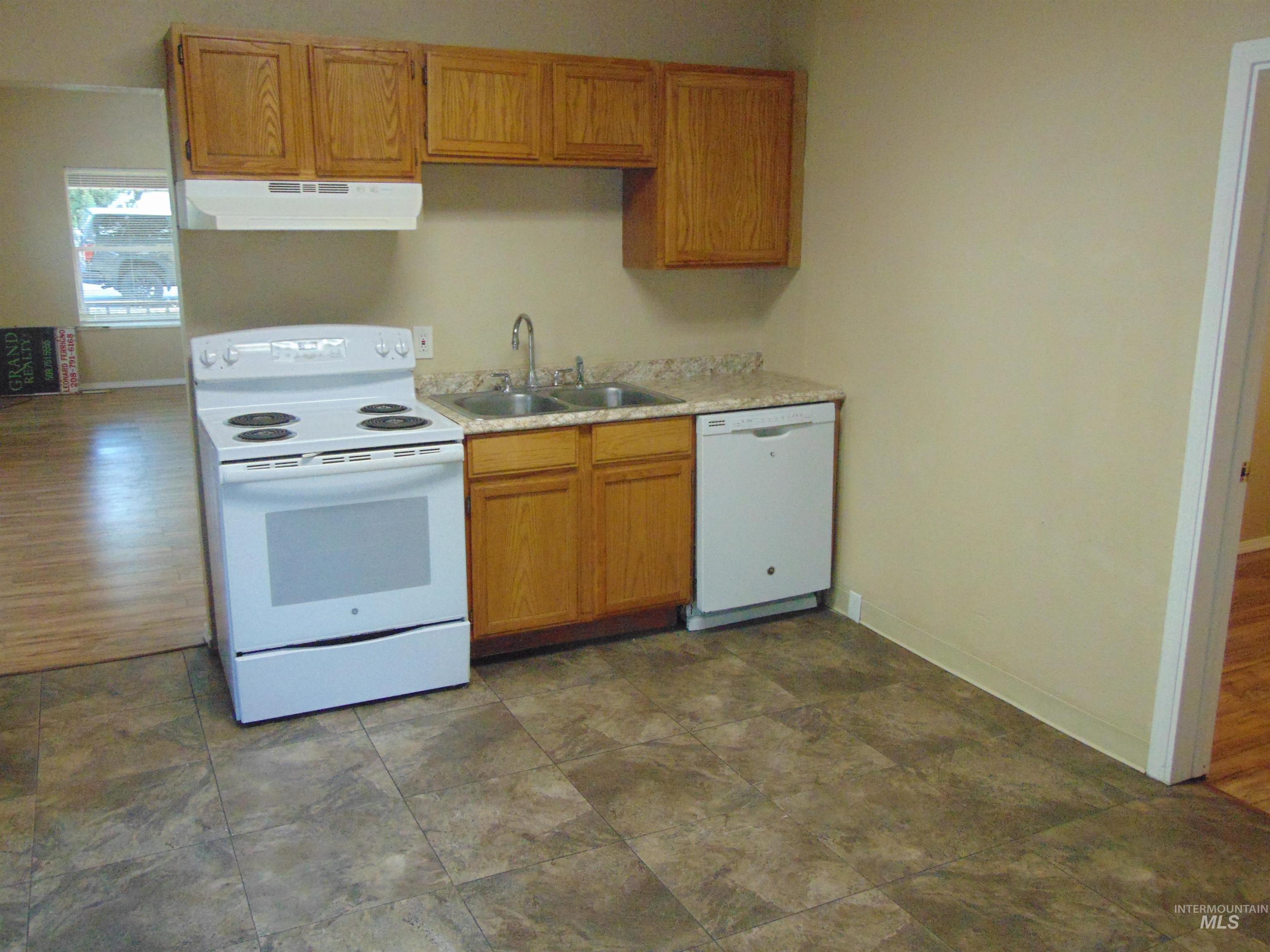 Kitchen with white appliances, light countertops, brown cabinetry, and under cabinet range hood