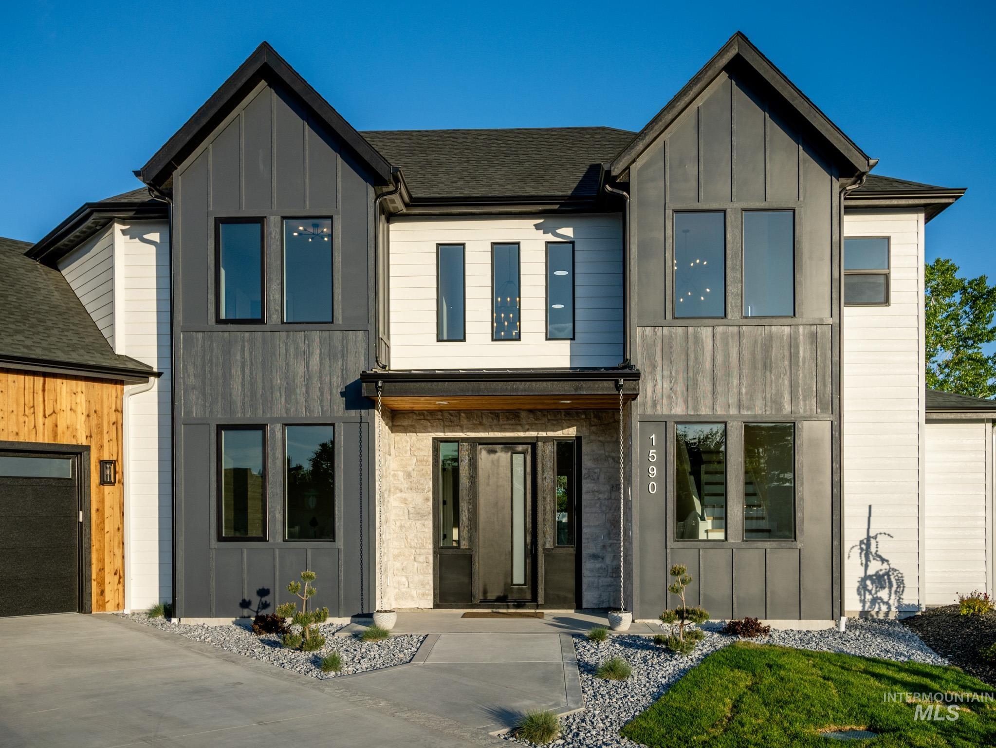 Contemporary house with board and batten siding, stone siding, a garage, and roof with shingles