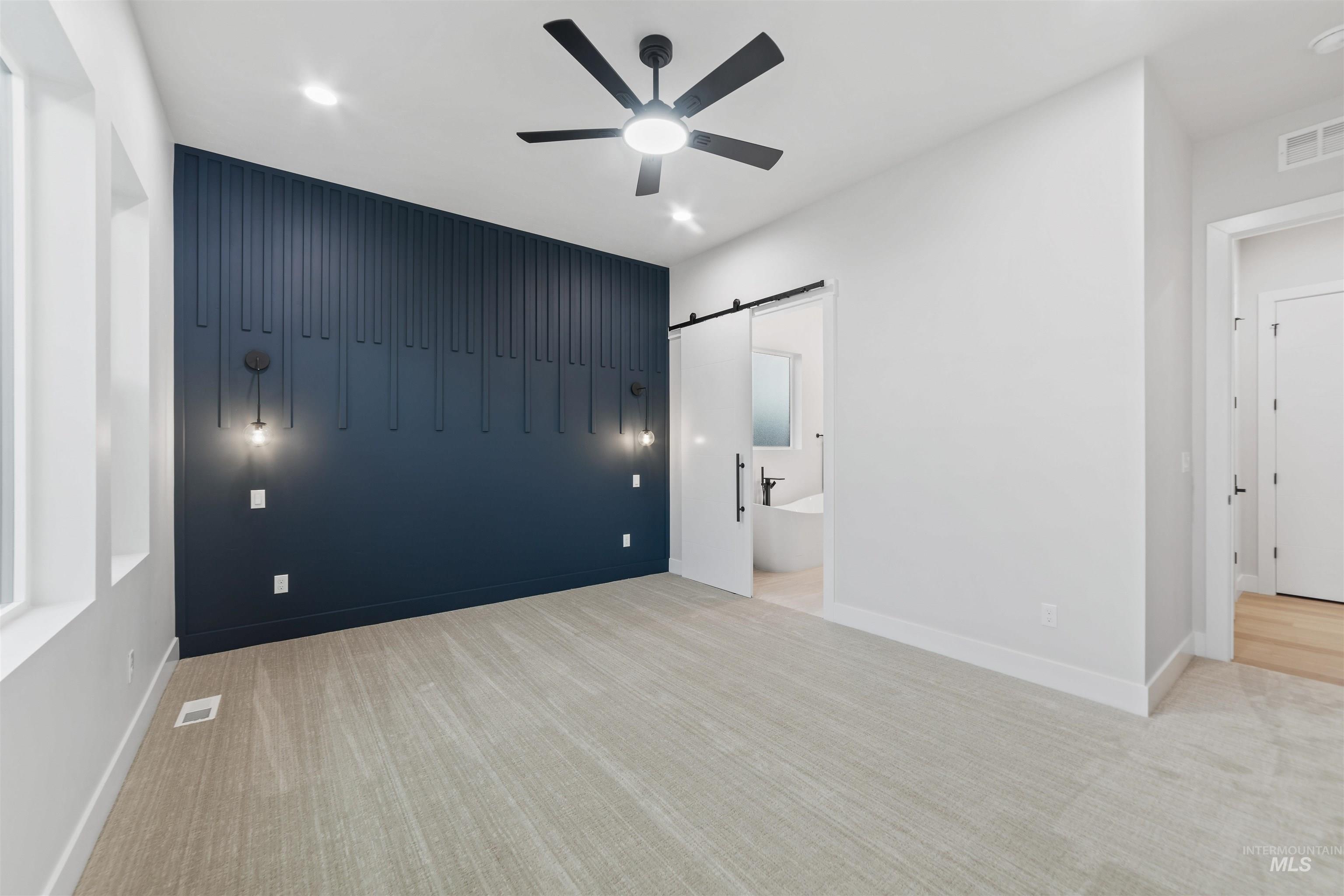 Unfurnished bedroom featuring a barn door, light carpet, a ceiling fan, recessed lighting, and connected bathroom