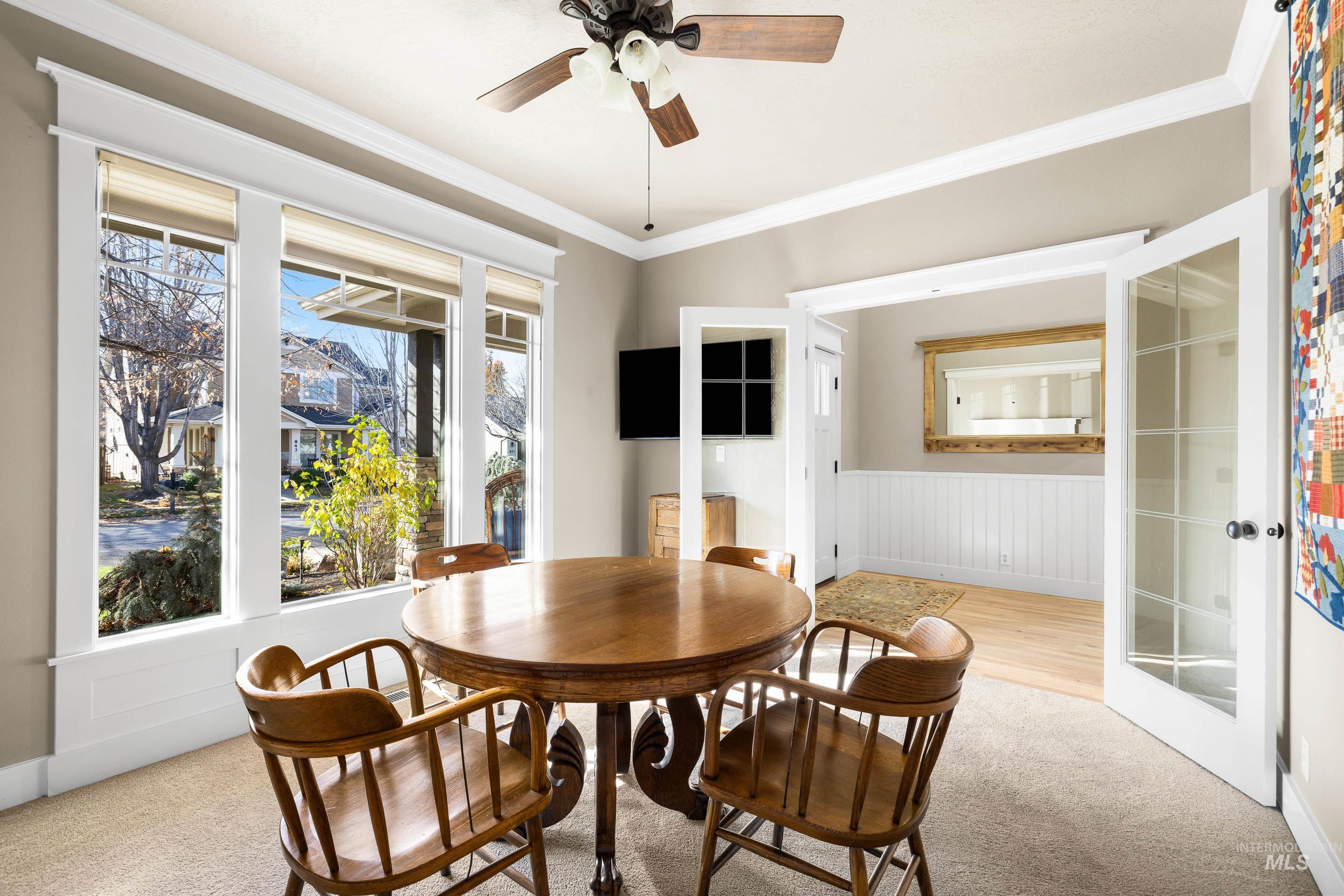 Dining room featuring light colored carpet, crown molding, ceiling fan, and wainscoting