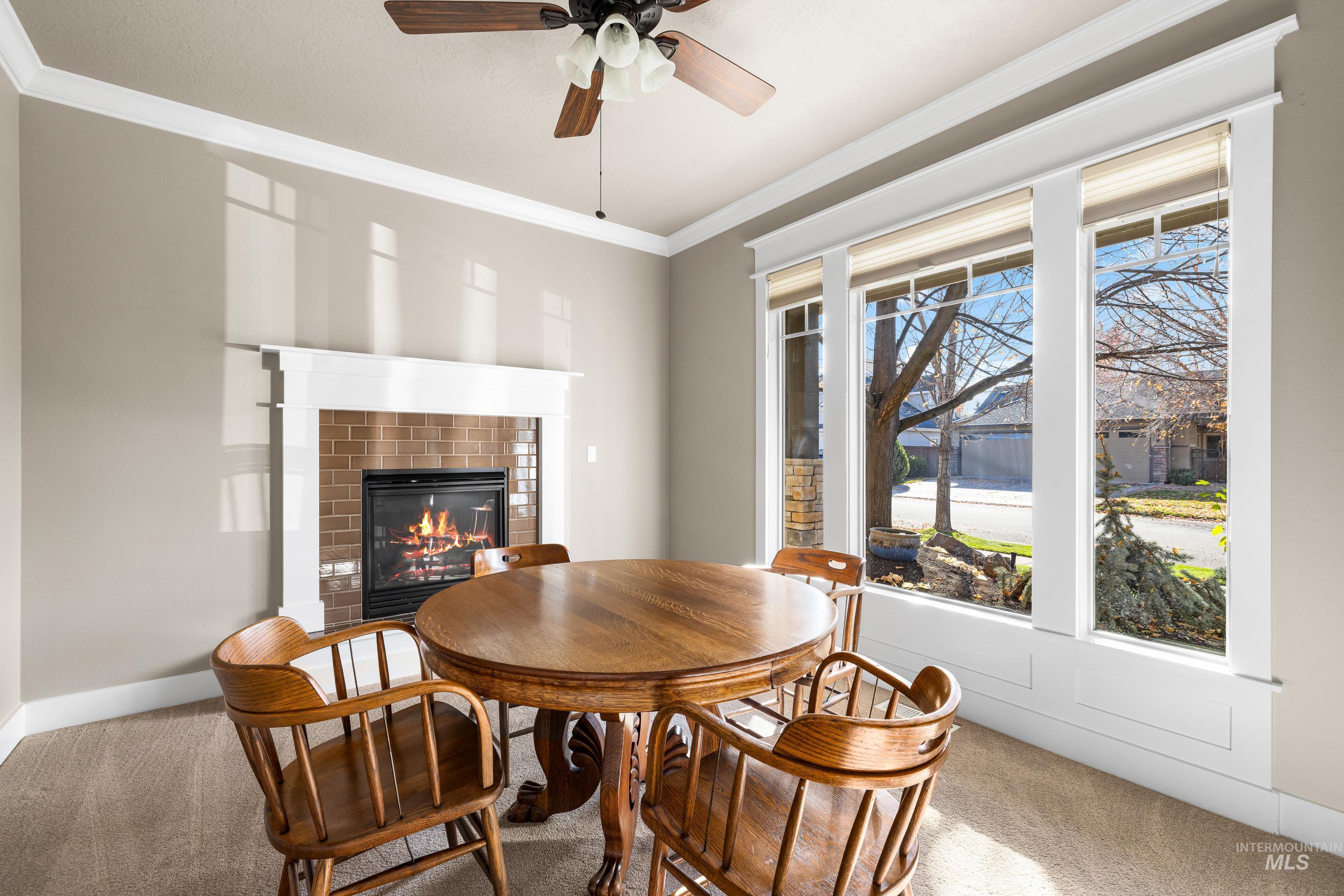 Dining area featuring carpet, ornamental molding, a glass covered fireplace, and a ceiling fan