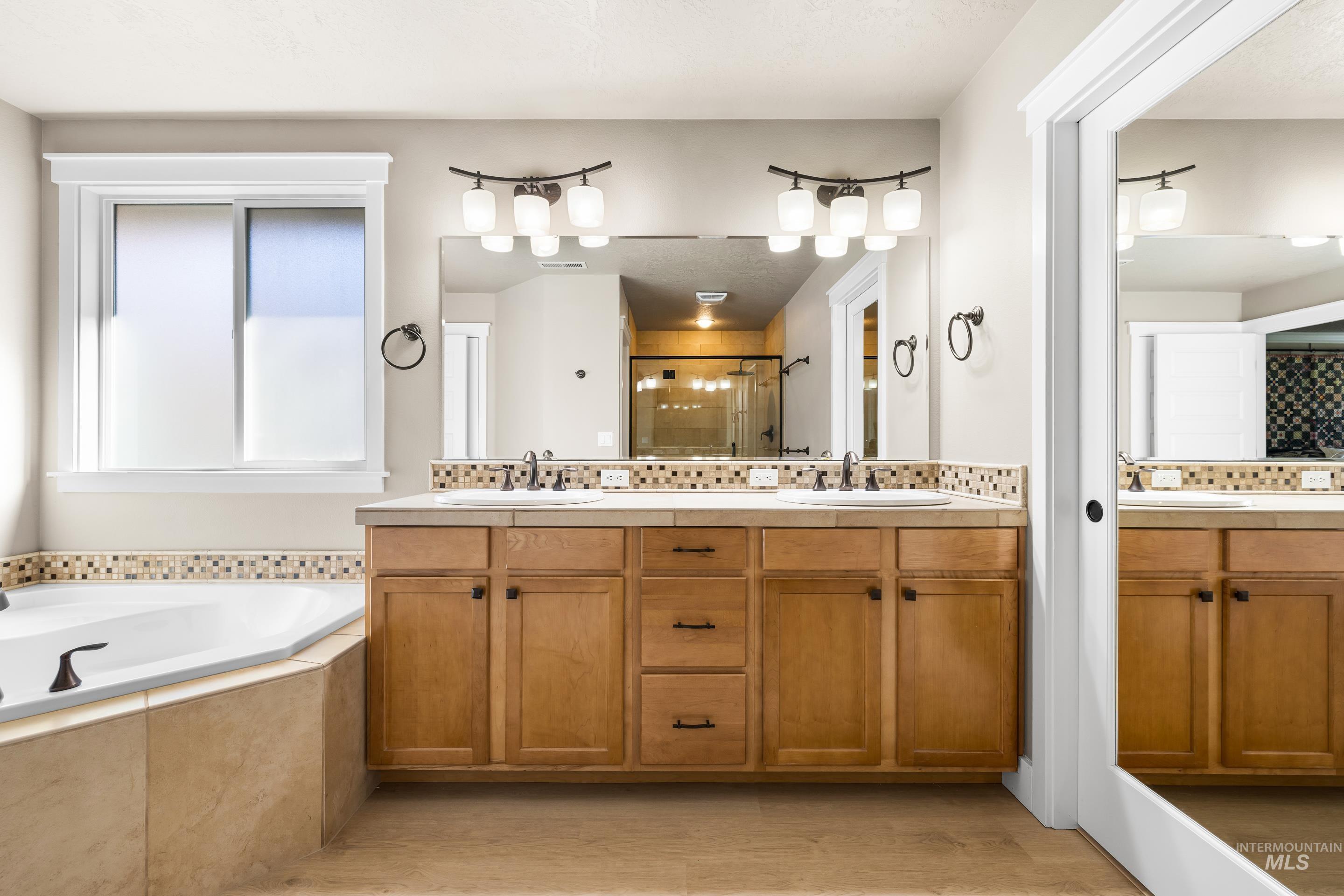 Full bathroom featuring double vanity, tasteful backsplash, a stall shower, and a garden tub