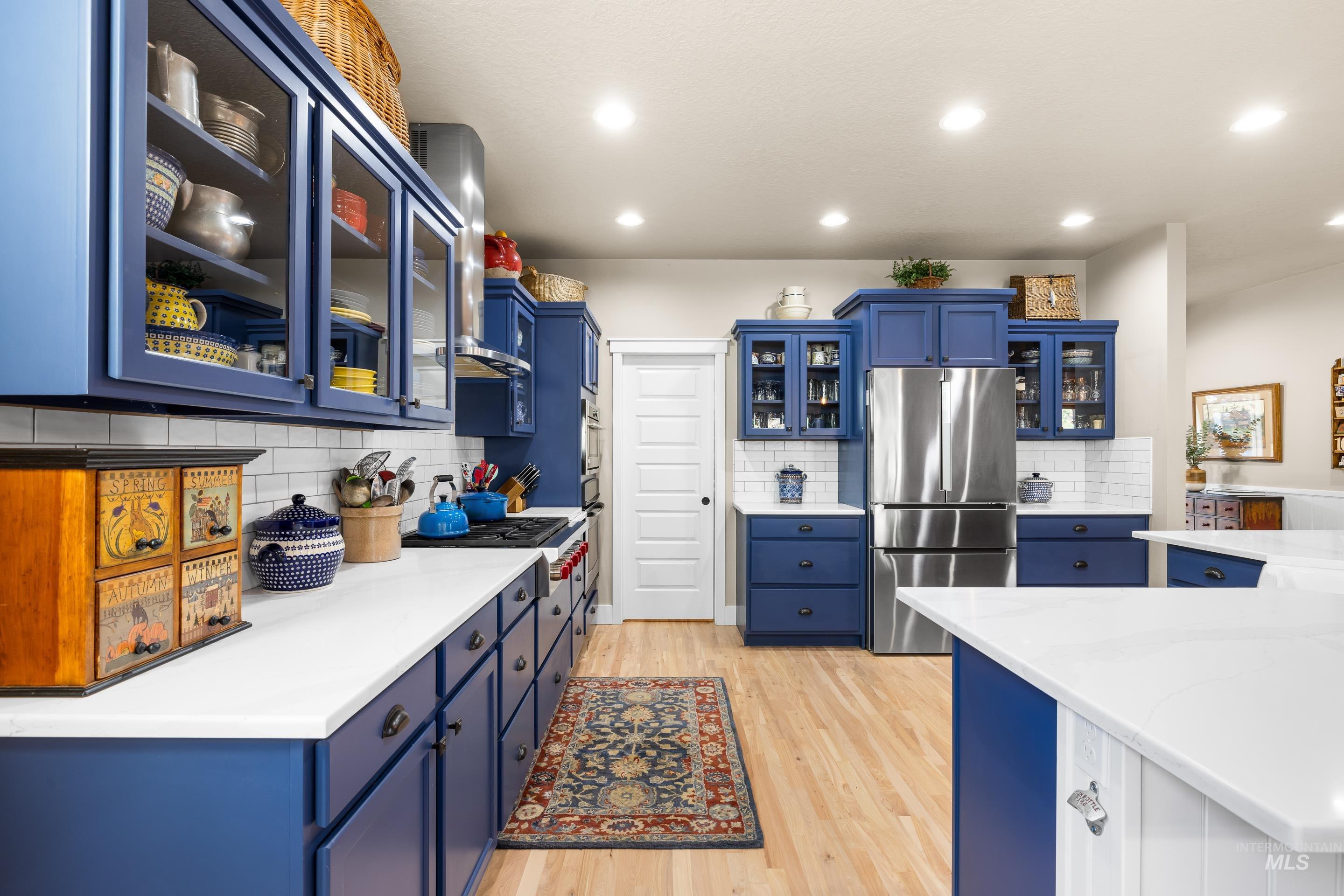 Kitchen with glass insert cabinets, blue cabinetry, stainless steel appliances, light wood-style floors, and recessed lighting