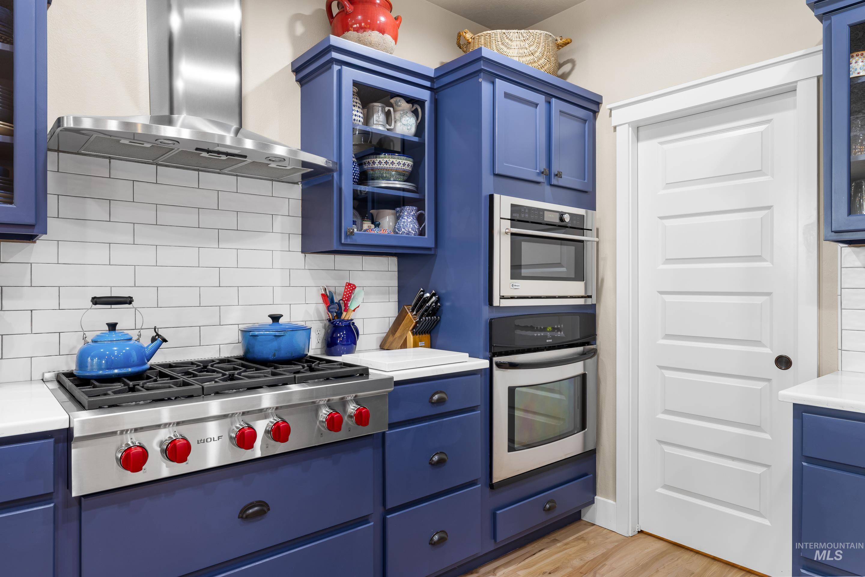 Kitchen featuring glass insert cabinets, blue cabinetry, decorative backsplash, extractor fan, and stainless steel appliances