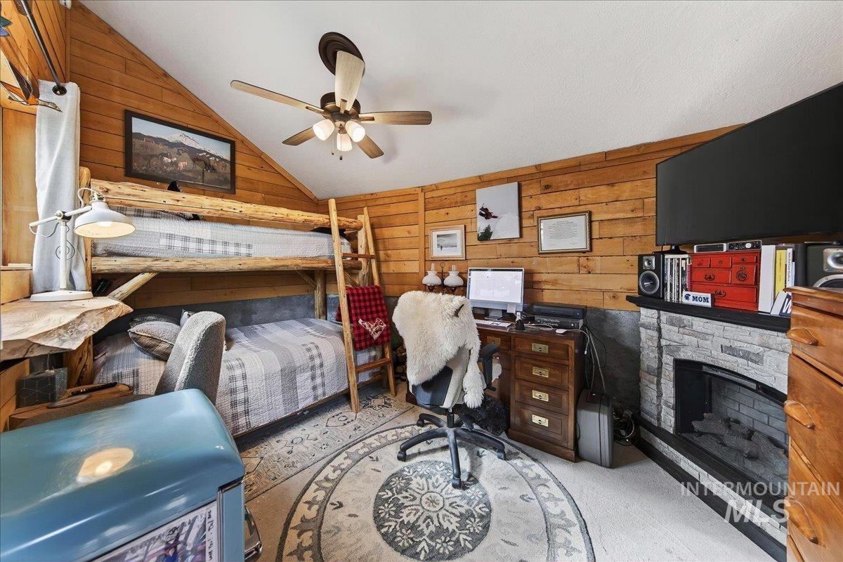 Bunkhouse with wood walls, a fireplace, light carpet, vaulted ceiling, and a ceiling fan