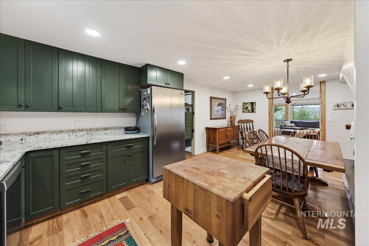 Kitchen featuring green cabinetry, a chandelier, freestanding refrigerator, light wood-style flooring, and light stone countertops