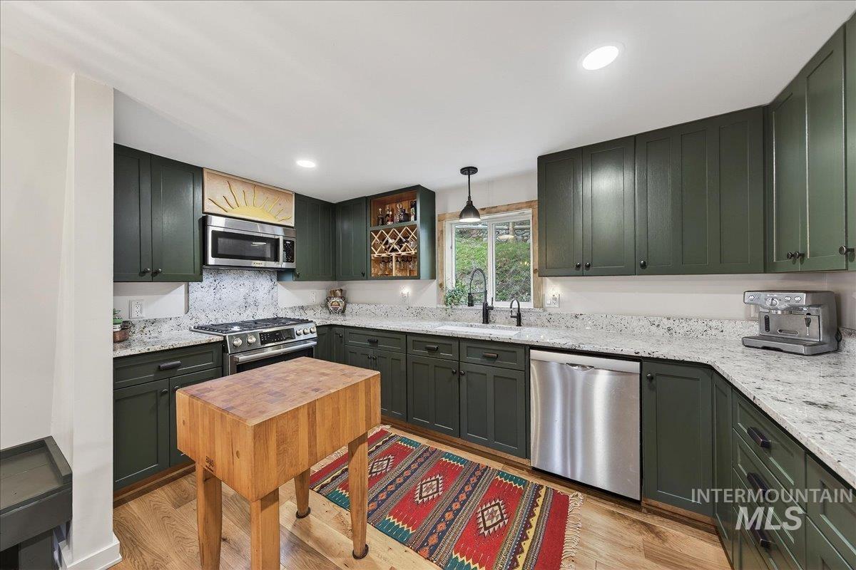 Kitchen with stainless steel appliances, light stone counters, light wood-style flooring, and green cabinets