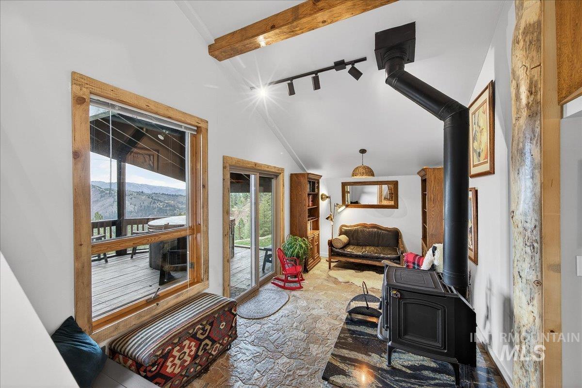 Living area featuring a wood stove, light stone finish floors, and vaulted ceiling with beams
